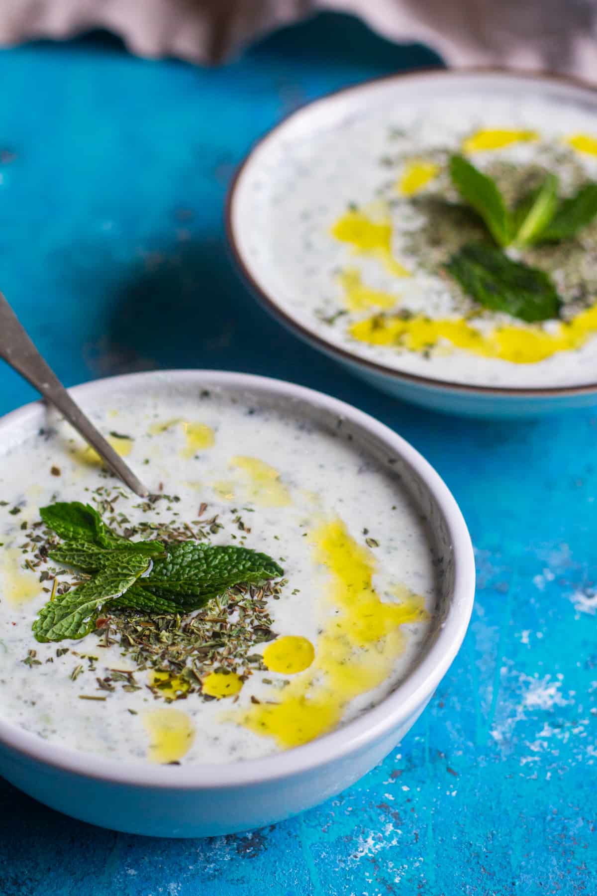 Two bowls of Turkish cacik on a blue surface