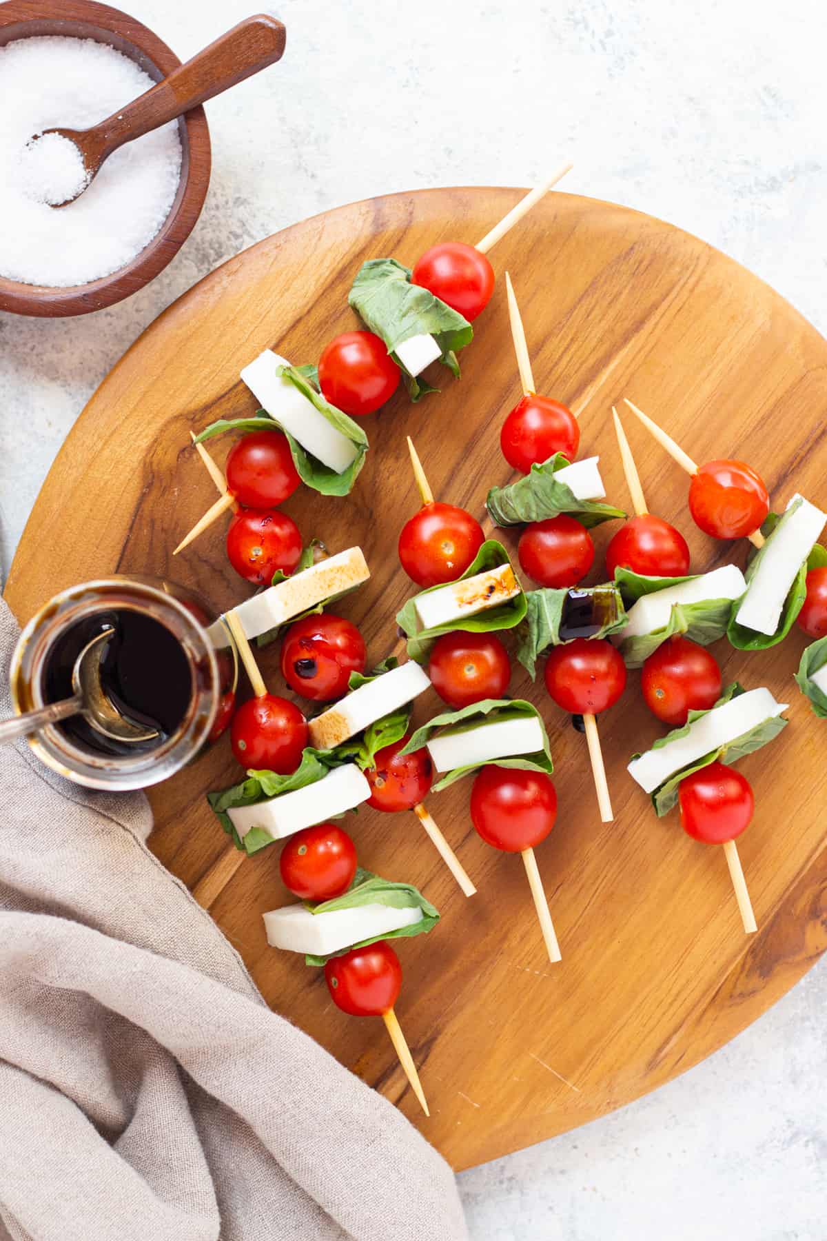 Caprese skewers on a wooden board with some salt and balsamic vinaigrette.