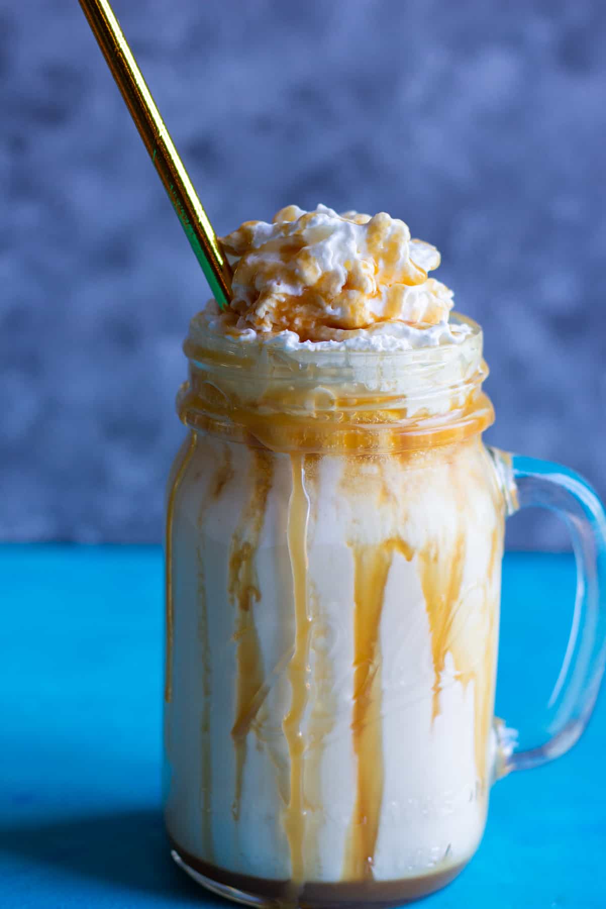A glass of caramel milkshake with whipped cream and a golden straw. 