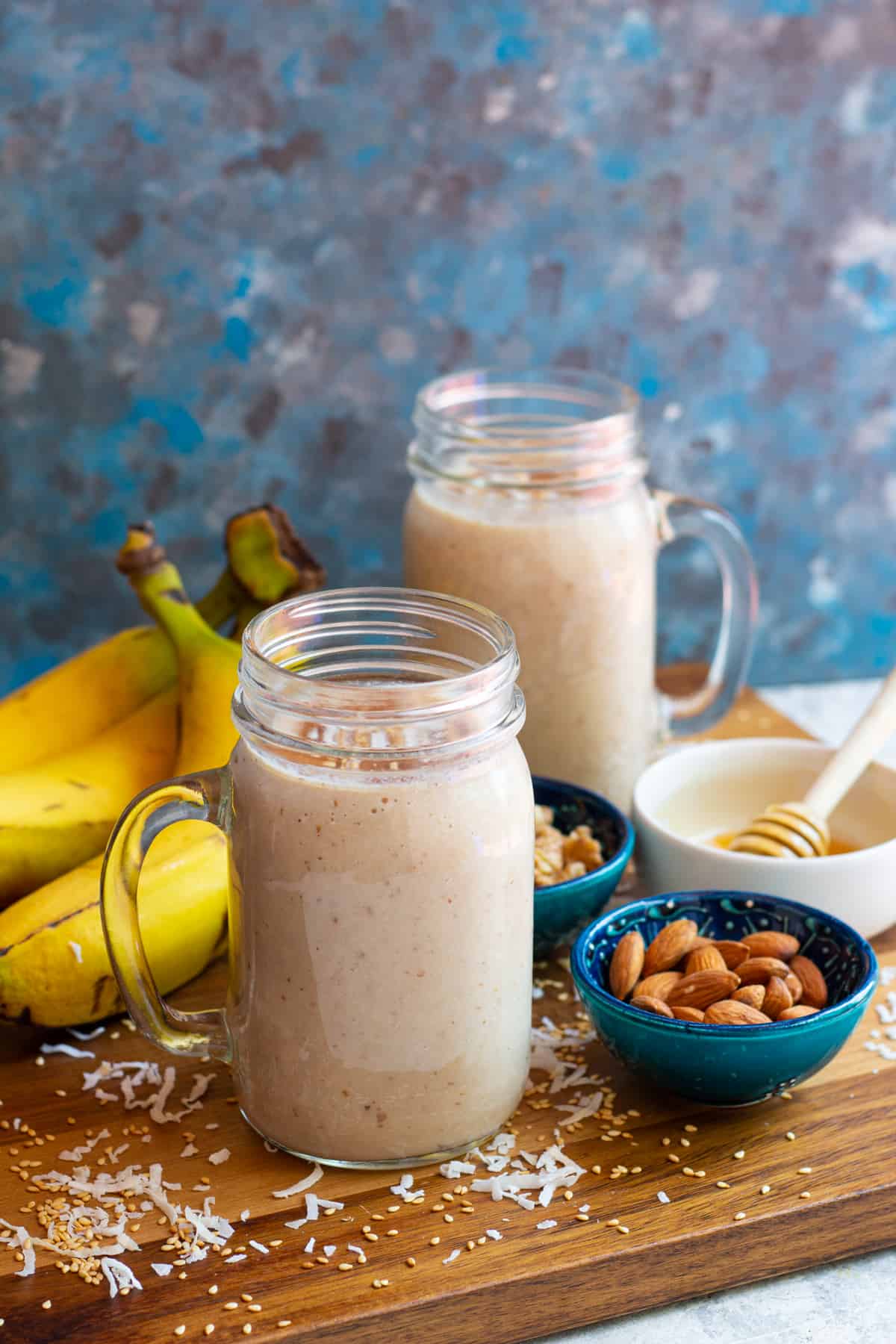 Two glasses of banana date shake with fruit and nuts on the background.