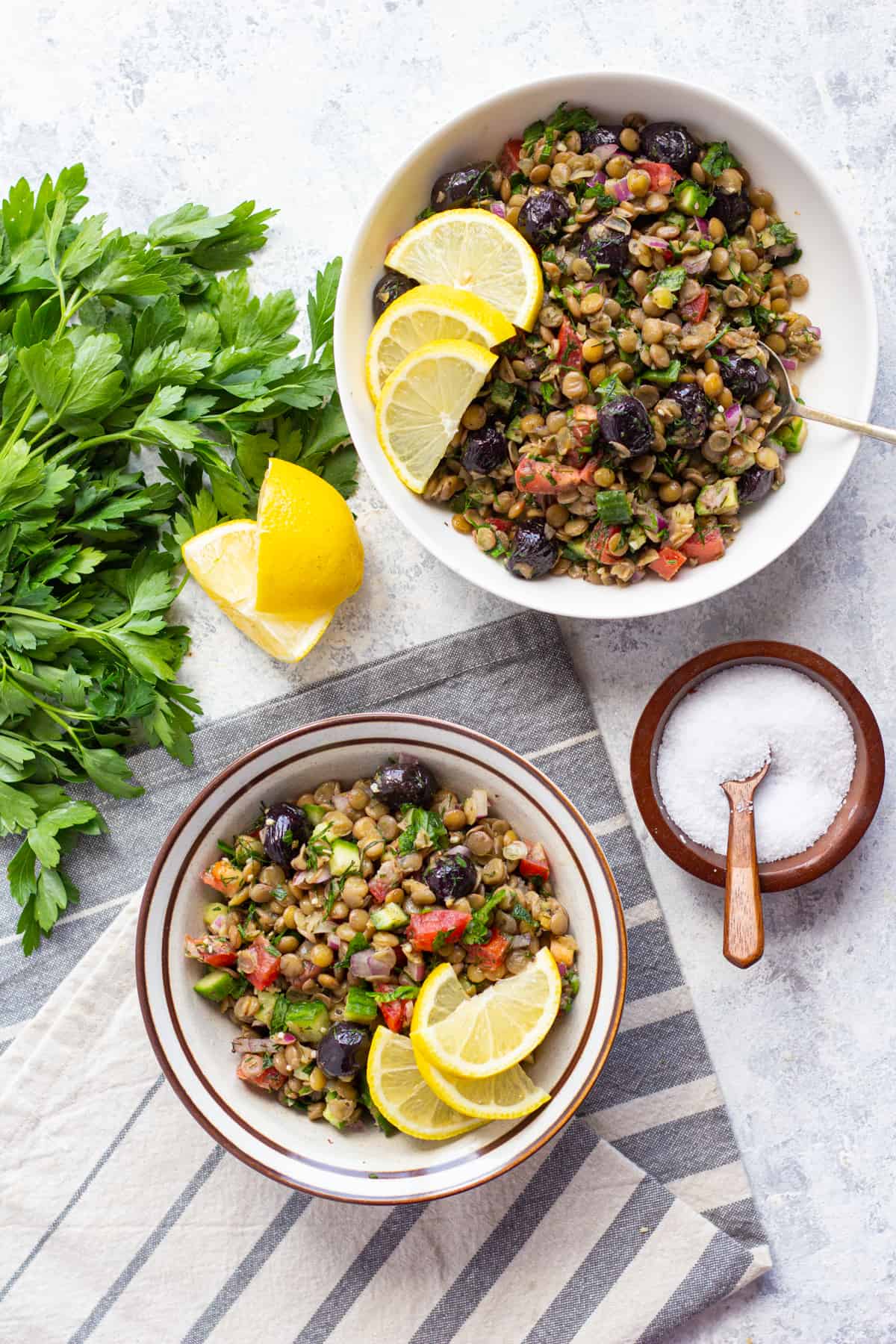 Two bowls of Greek lentil salad with lemon slices and a bunch of parsley. 