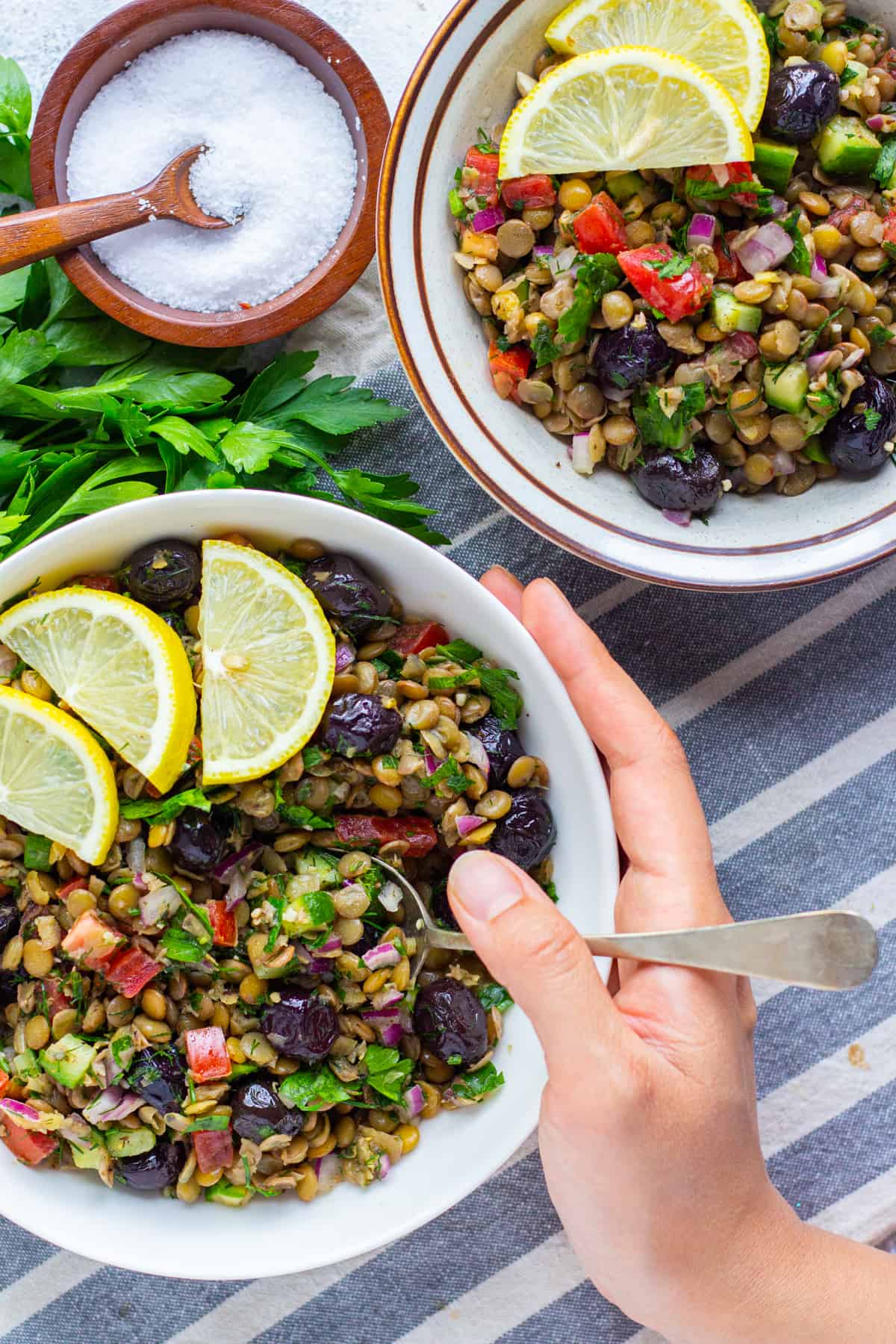 close up shot of two bowls of cold salad with lemon slices and a cup of salt. 