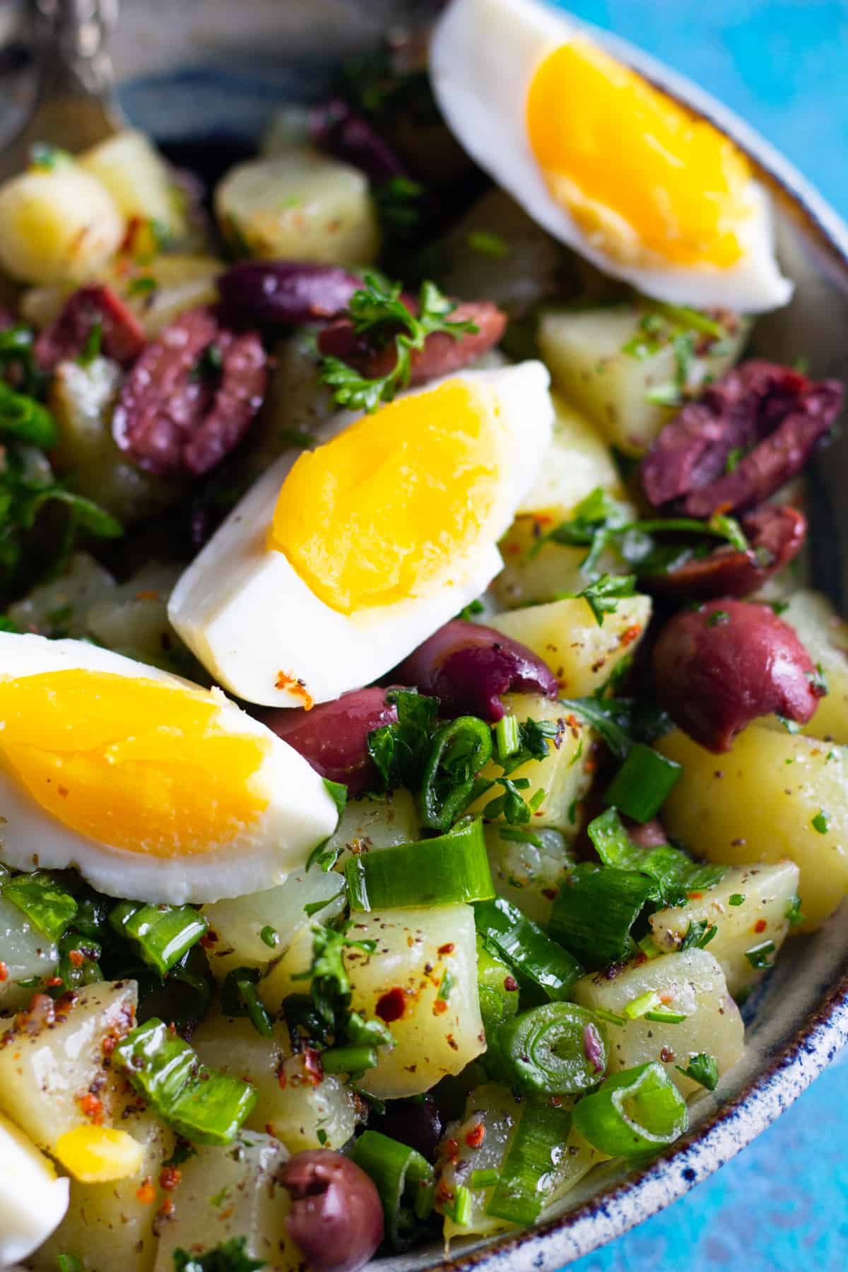 bowl of salad made with potatoes, eggs, herbs and olives