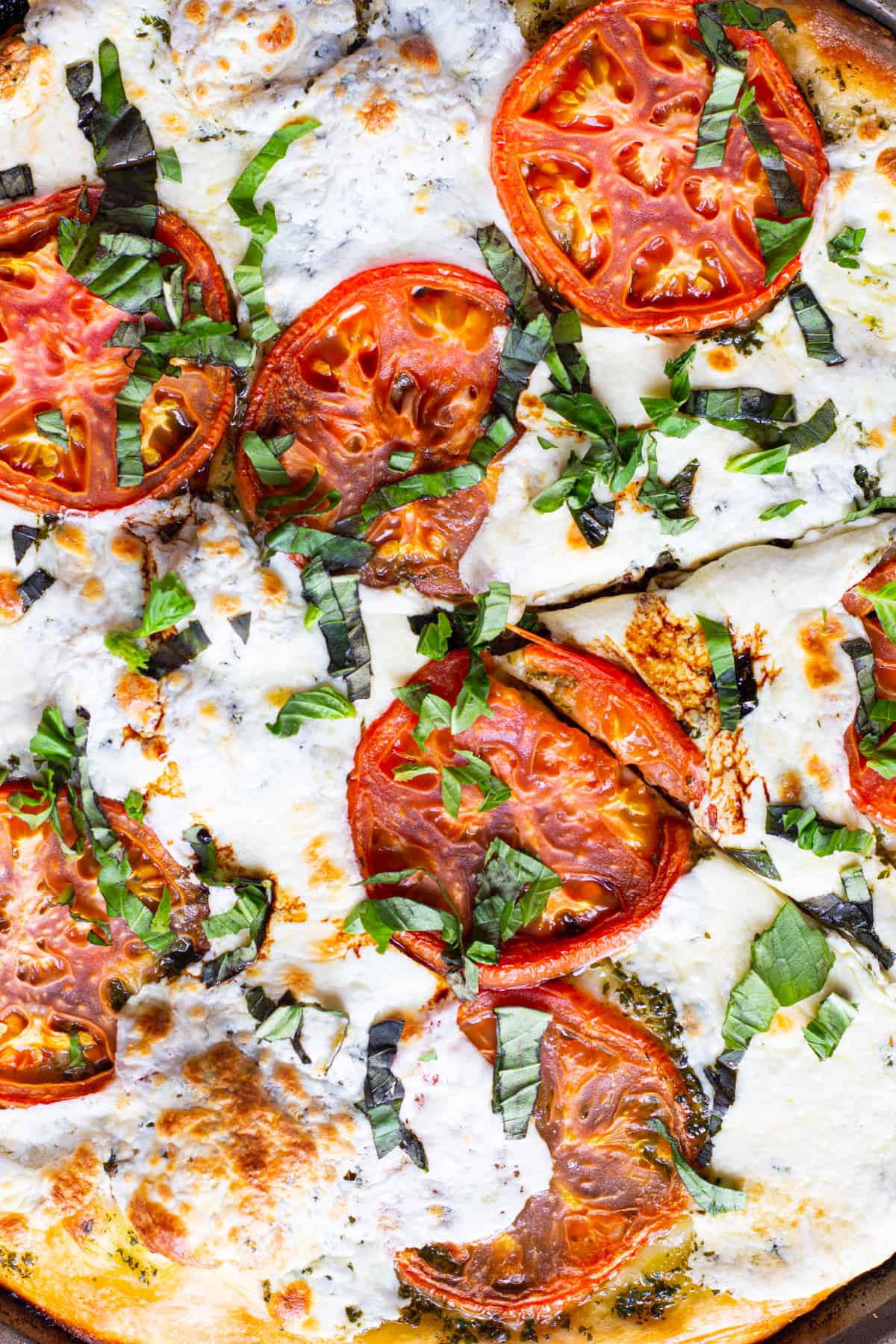 slices of tomato and mozzarella on pizza dough topped with basil leaves. 