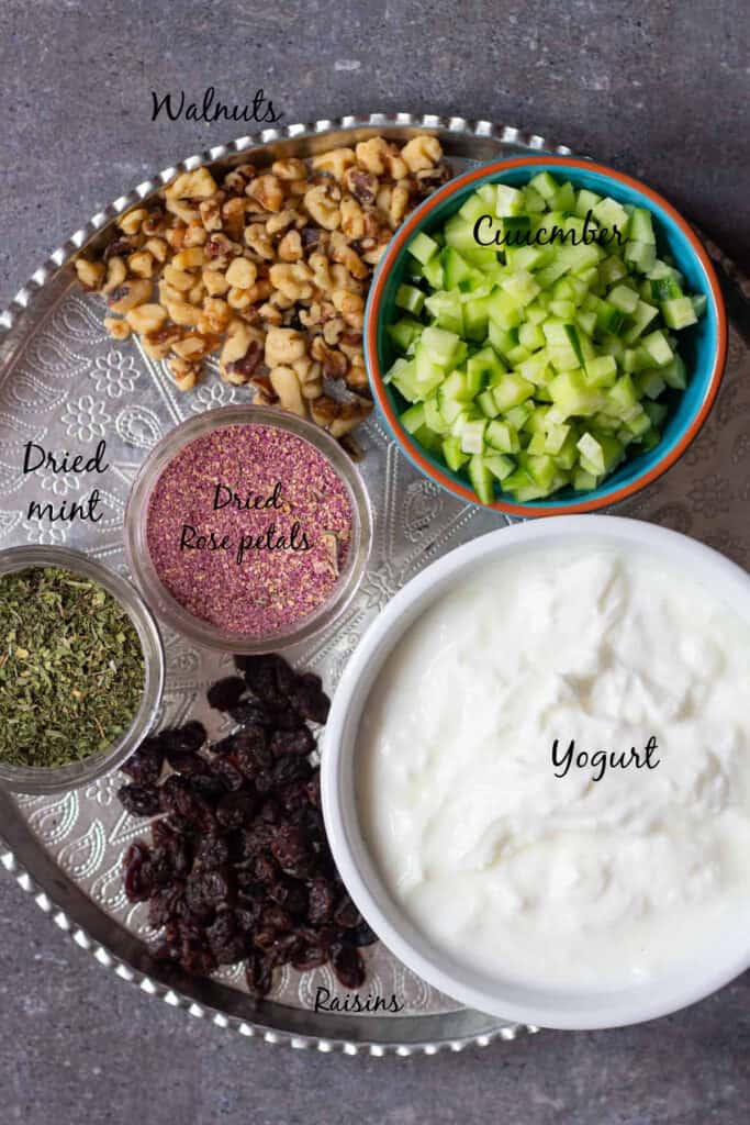 To make this yogurt dip we need cucumbers, yogurt, walnuts, raisins, rose petals and dried mint.