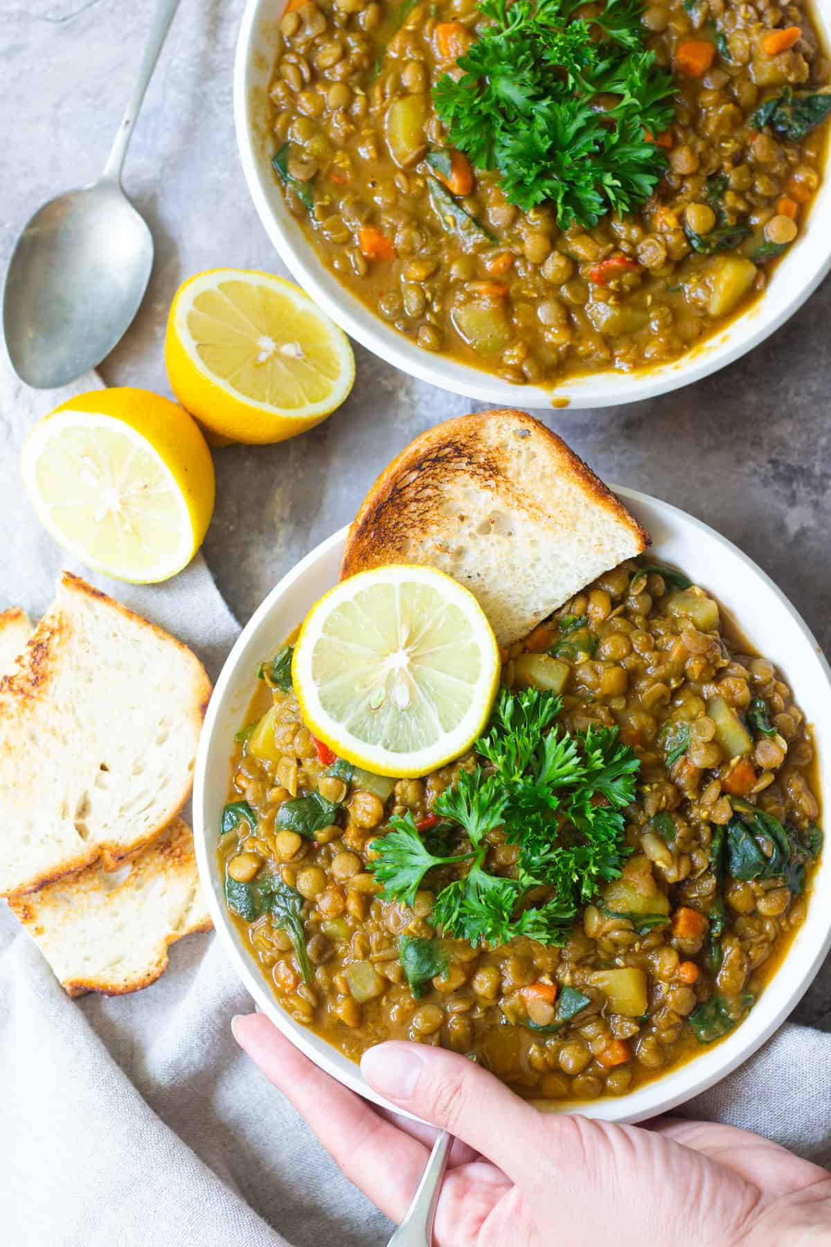 Two bowl of soup on a grey backdrop. Served with some toasted bread and lemon and topped with parsley. 