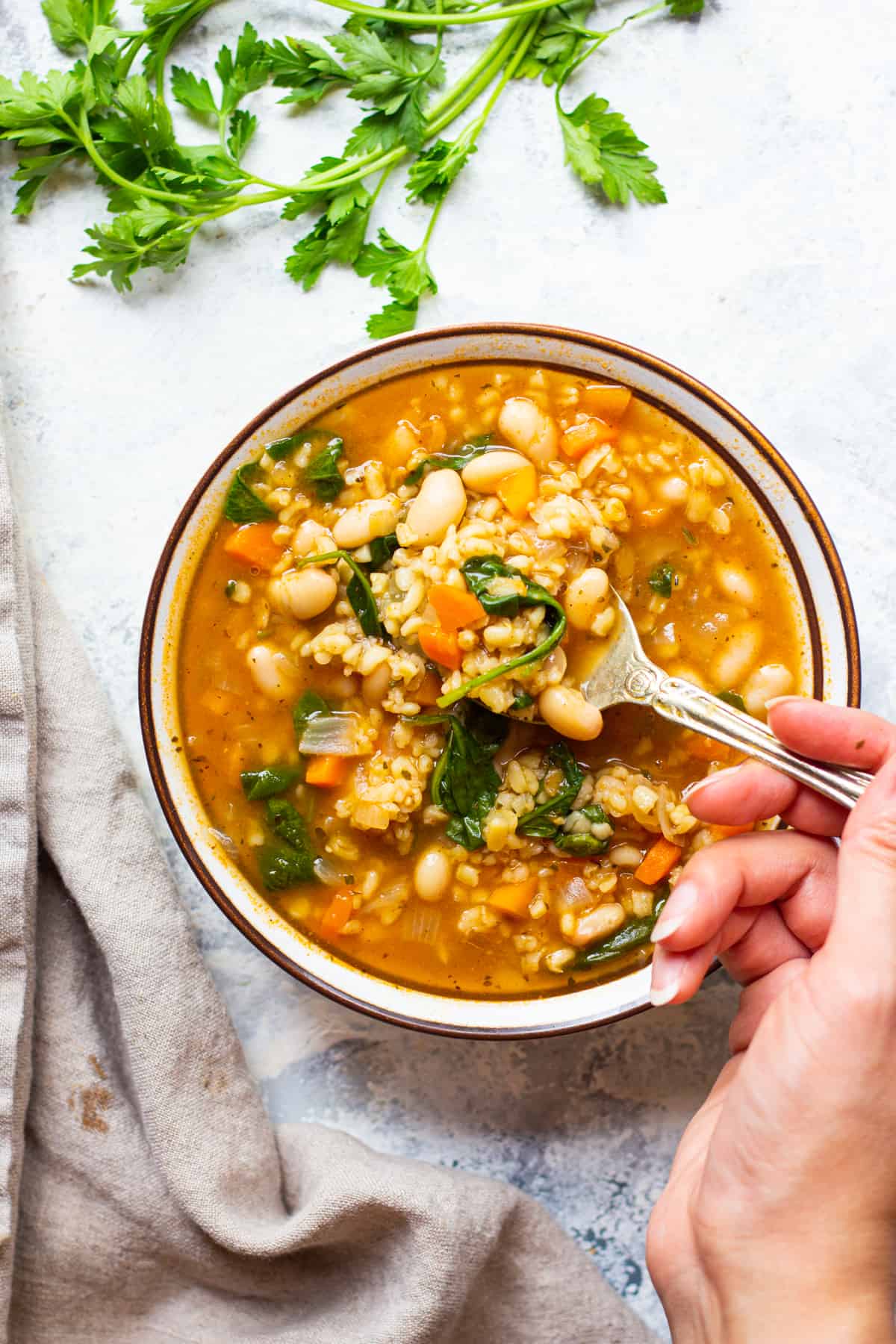 a spoon in the bowl of instant pot vegetable soup on a white surface with herbs.