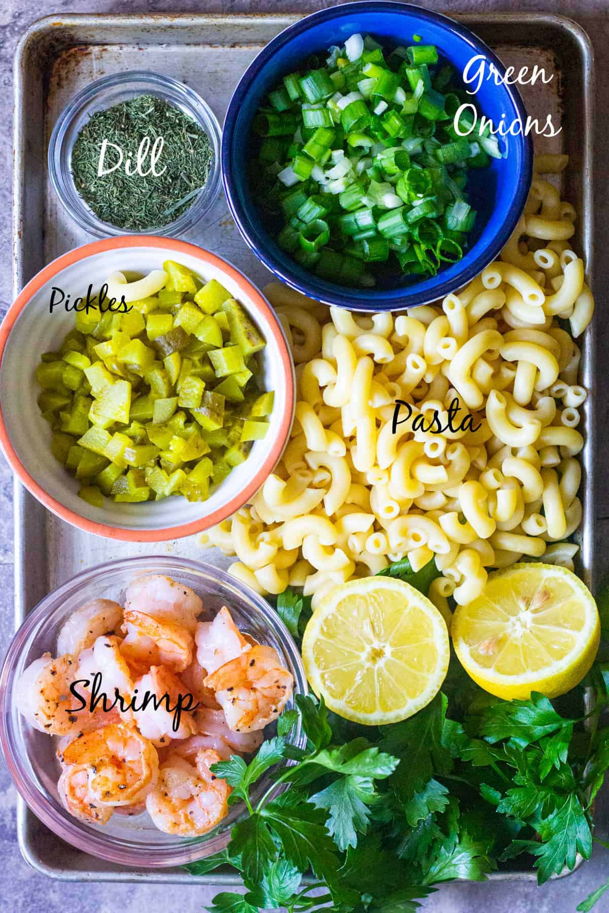 shrimp macaroni salad ingredients are cooked shrimp, pasta, parsley, dill, dill pickles, green onion, and lemon.