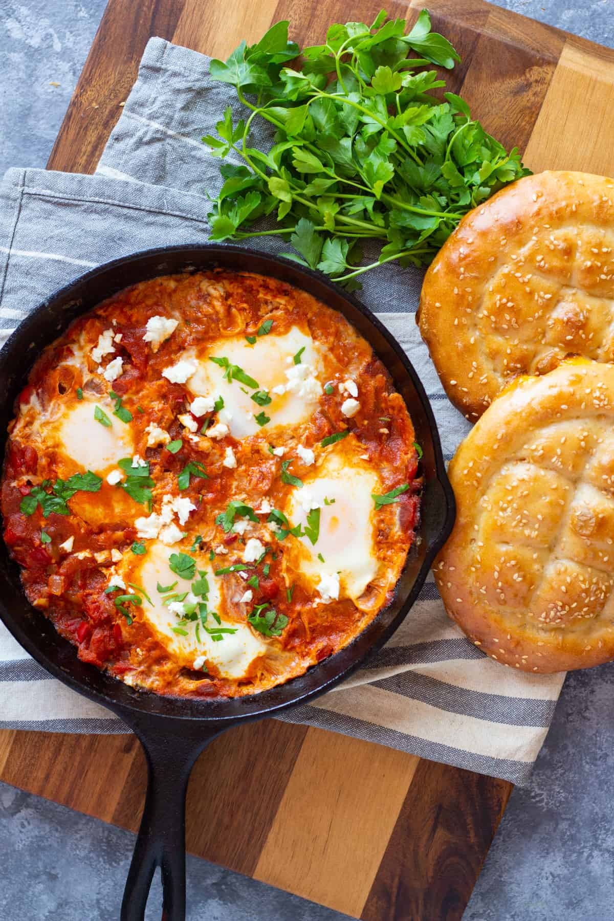 Overhead shot of the poached eggs in tomato sauce in a pan with bread and parsley. 