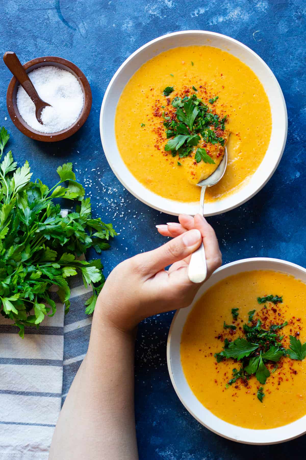 Two bowls of mercimek corbasi red lentil soup topped with parsley and Aleppo pepper. 
