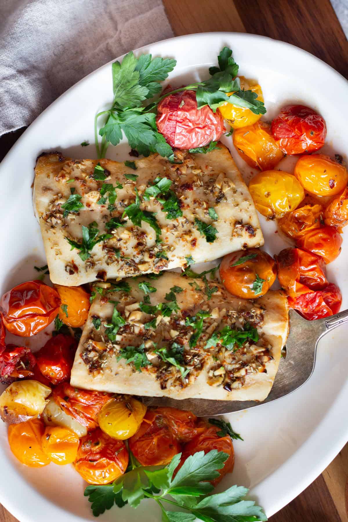 Two pieces of mahi mahi on a platter with tomatoes and herbs.
