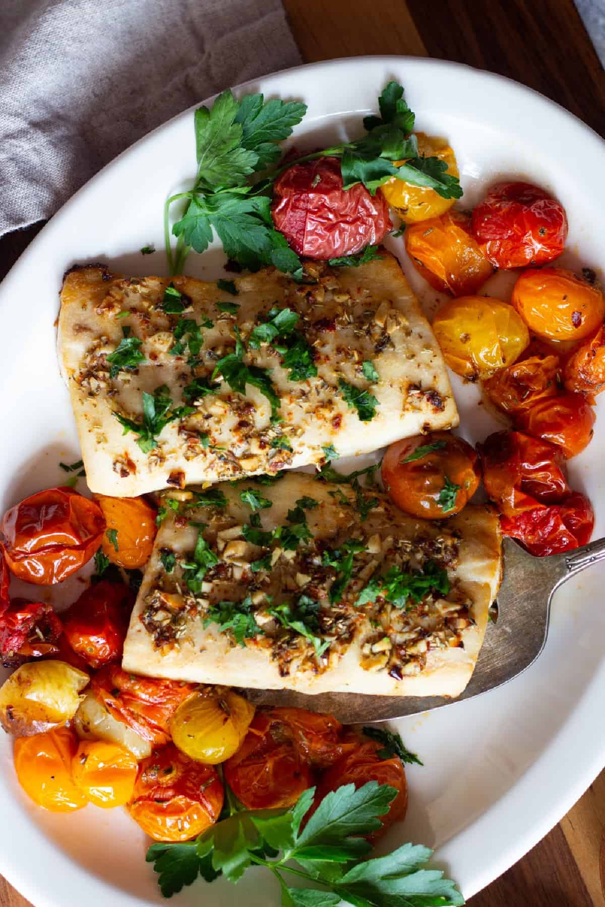 Two pieces of mahi mahi on a platter with tomatoes and herbs.