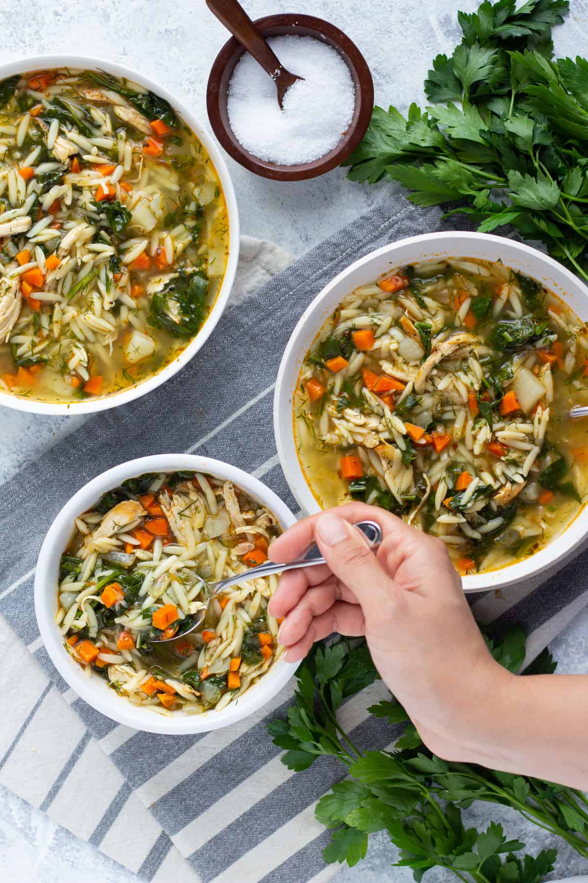 Three bowls of lemon orzo soup with chicken and spinach. 