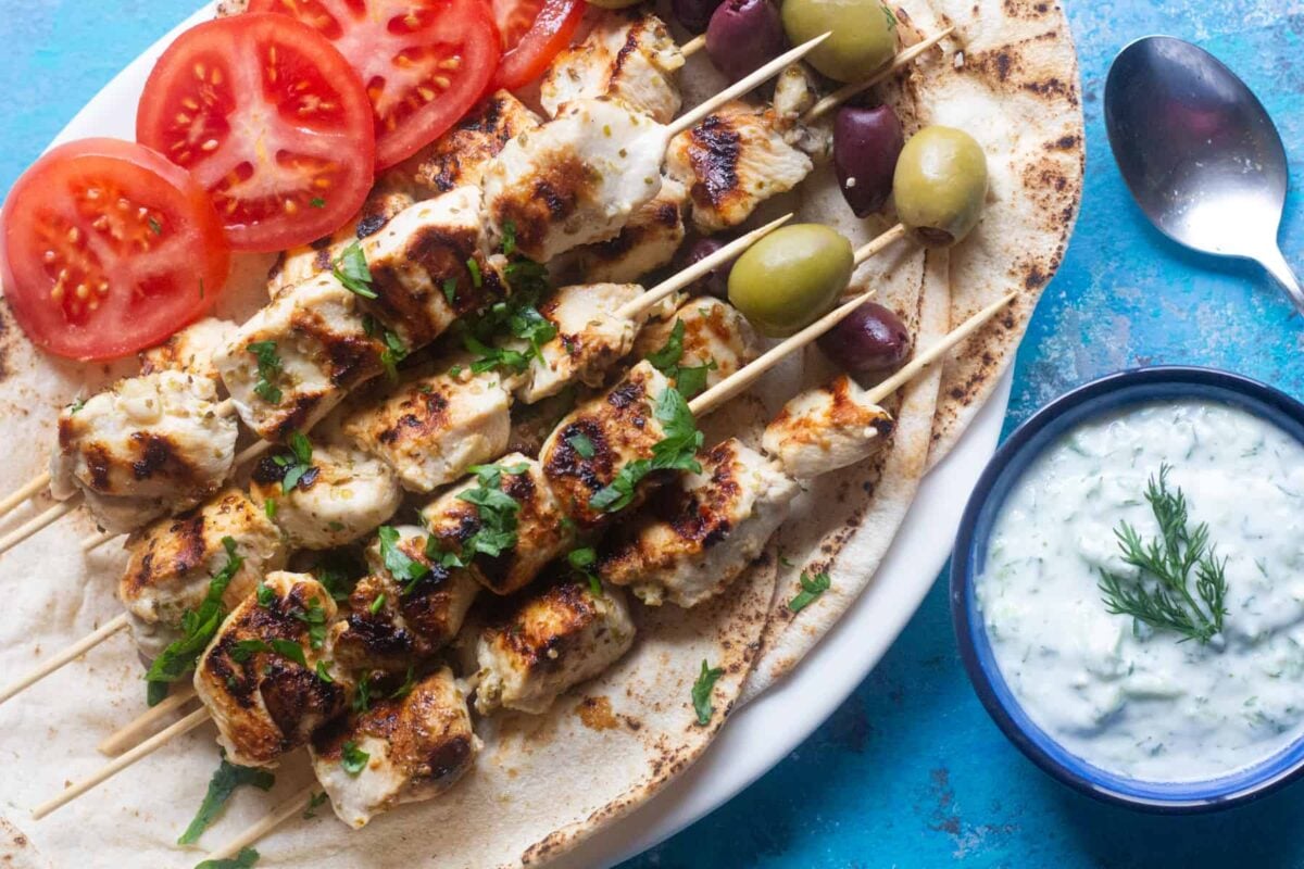 Overhead shot of Greek chicken souvlaki on a platter with pita and tzatziki. 