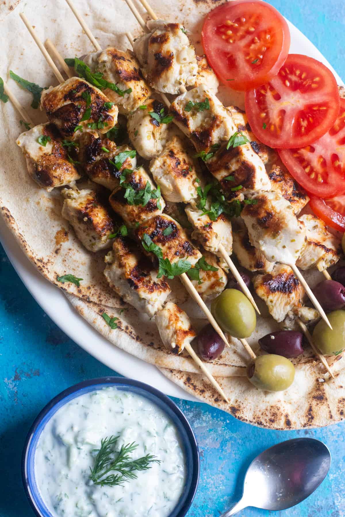 Chicken souvlaki on a platter with olives and bread. 