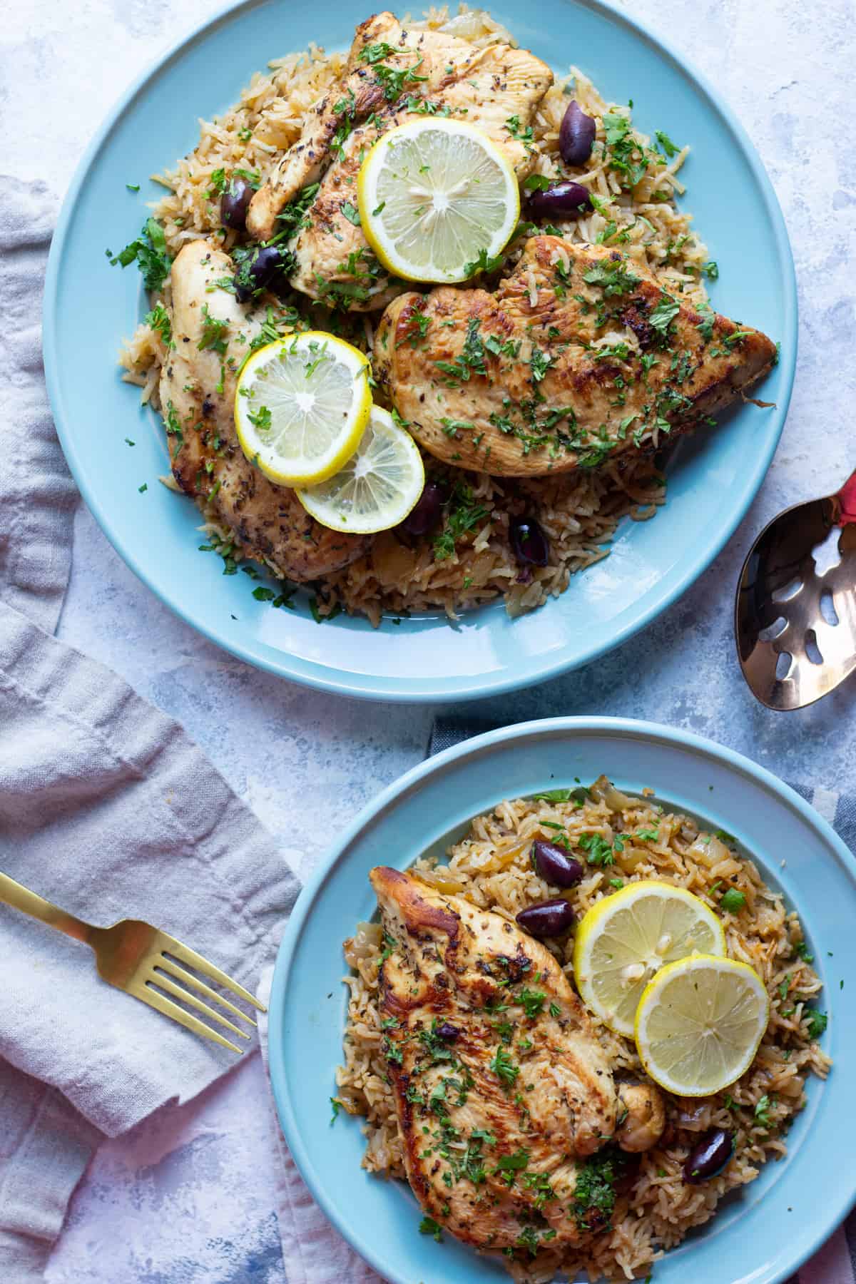 Two plates of chicken and rice with lemon and olives.