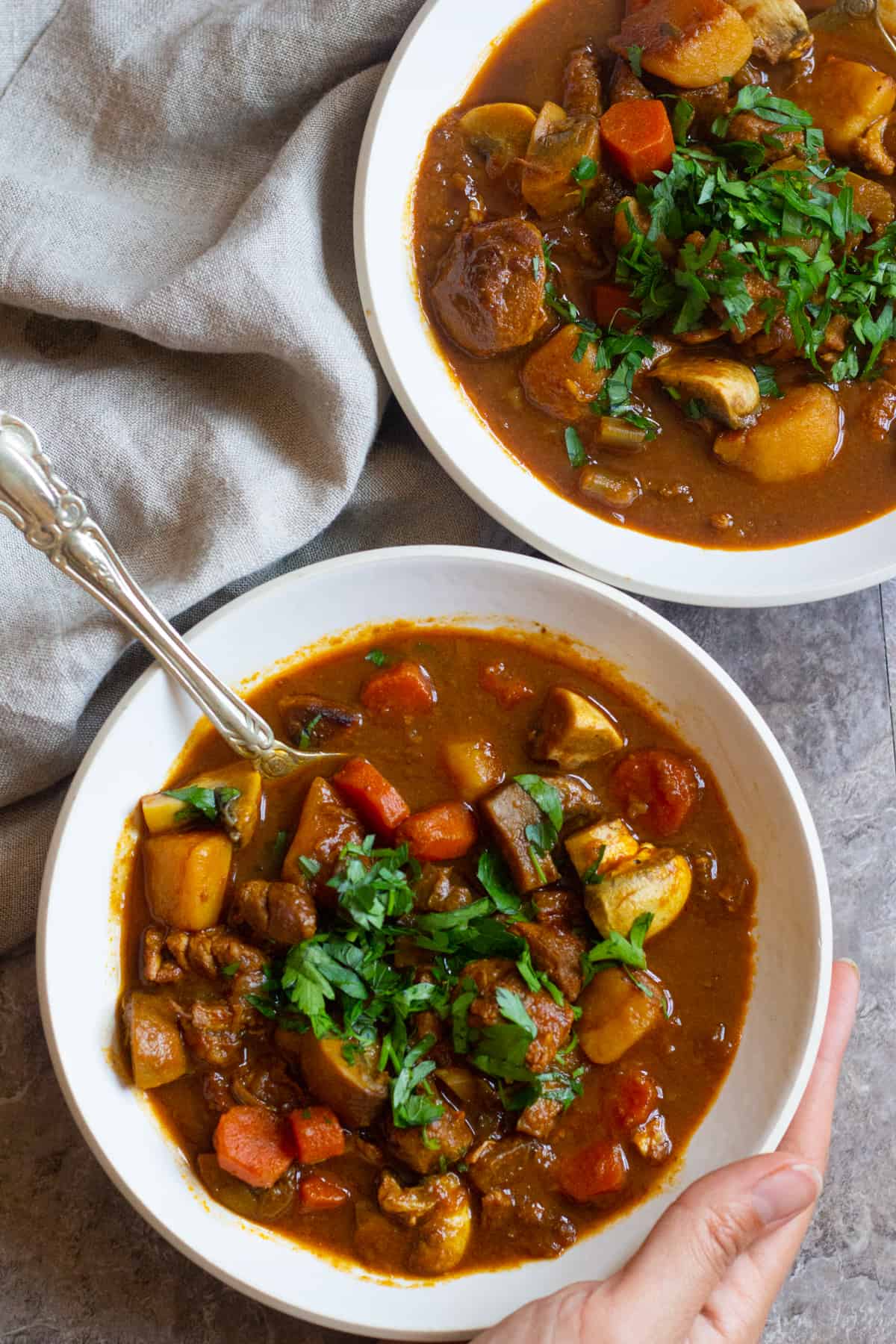 Two bowls of lamb stew on a grey backdrop. 