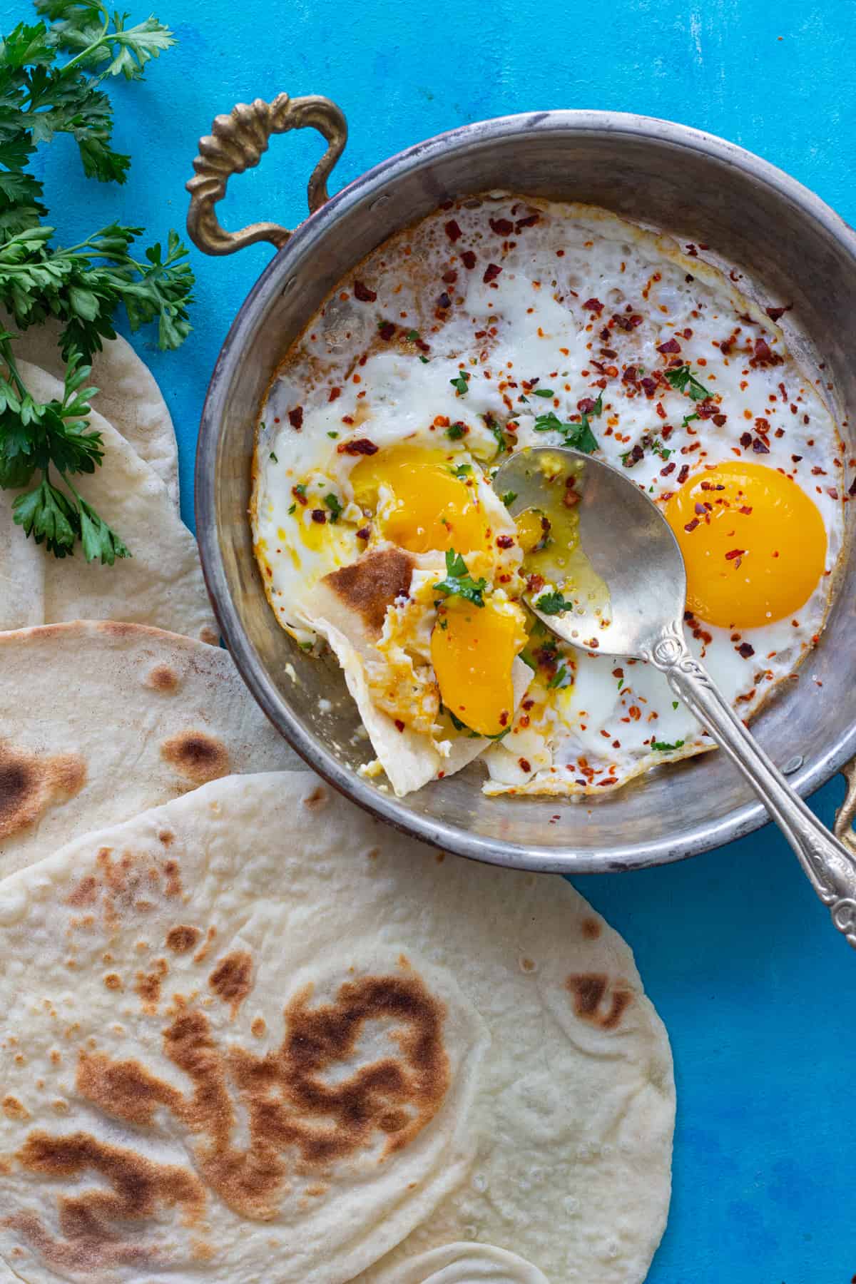 A pan of fried eggs with some parsley and bread.