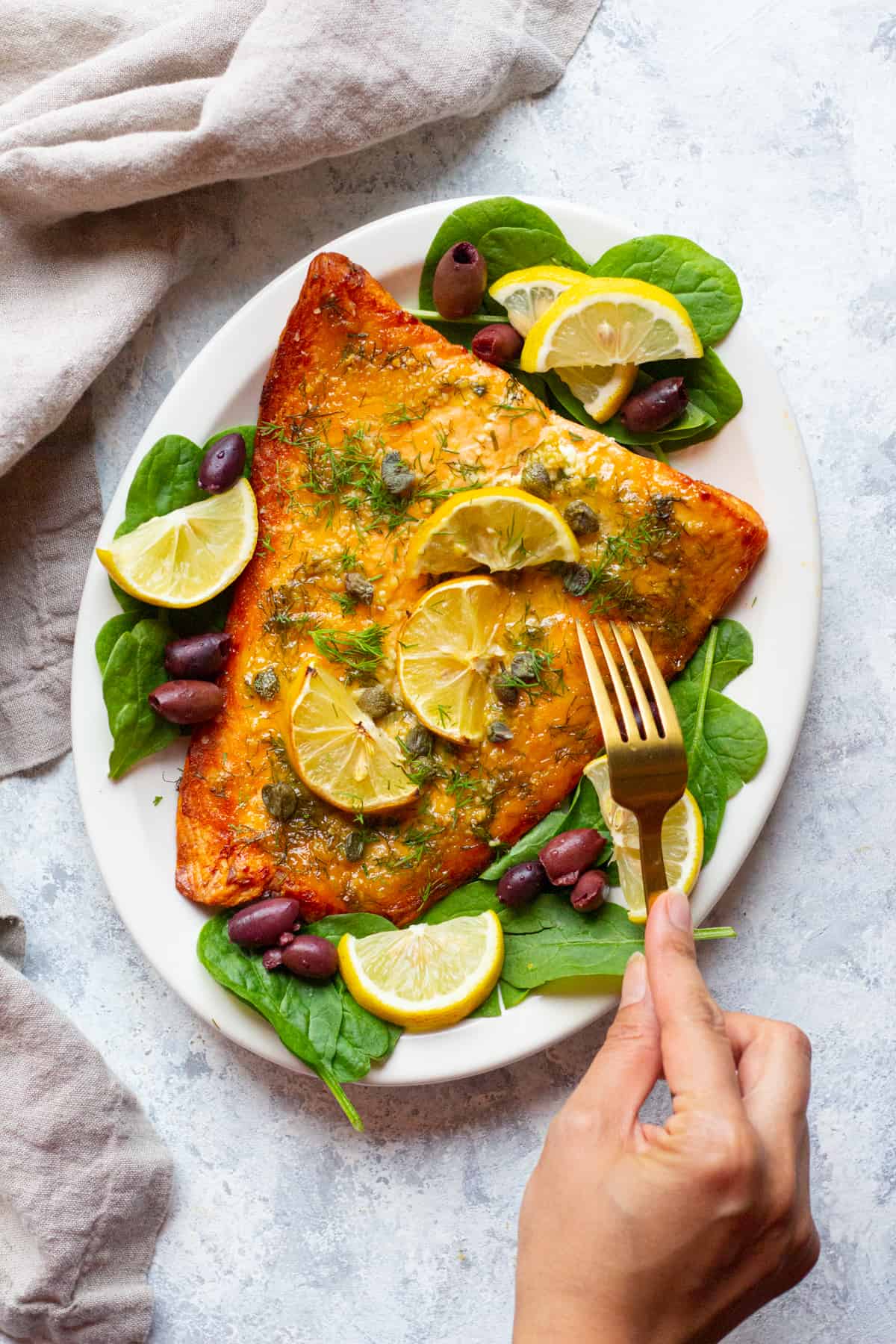 baked salmon with dijon mustard on a white plate with lemon and olives. 