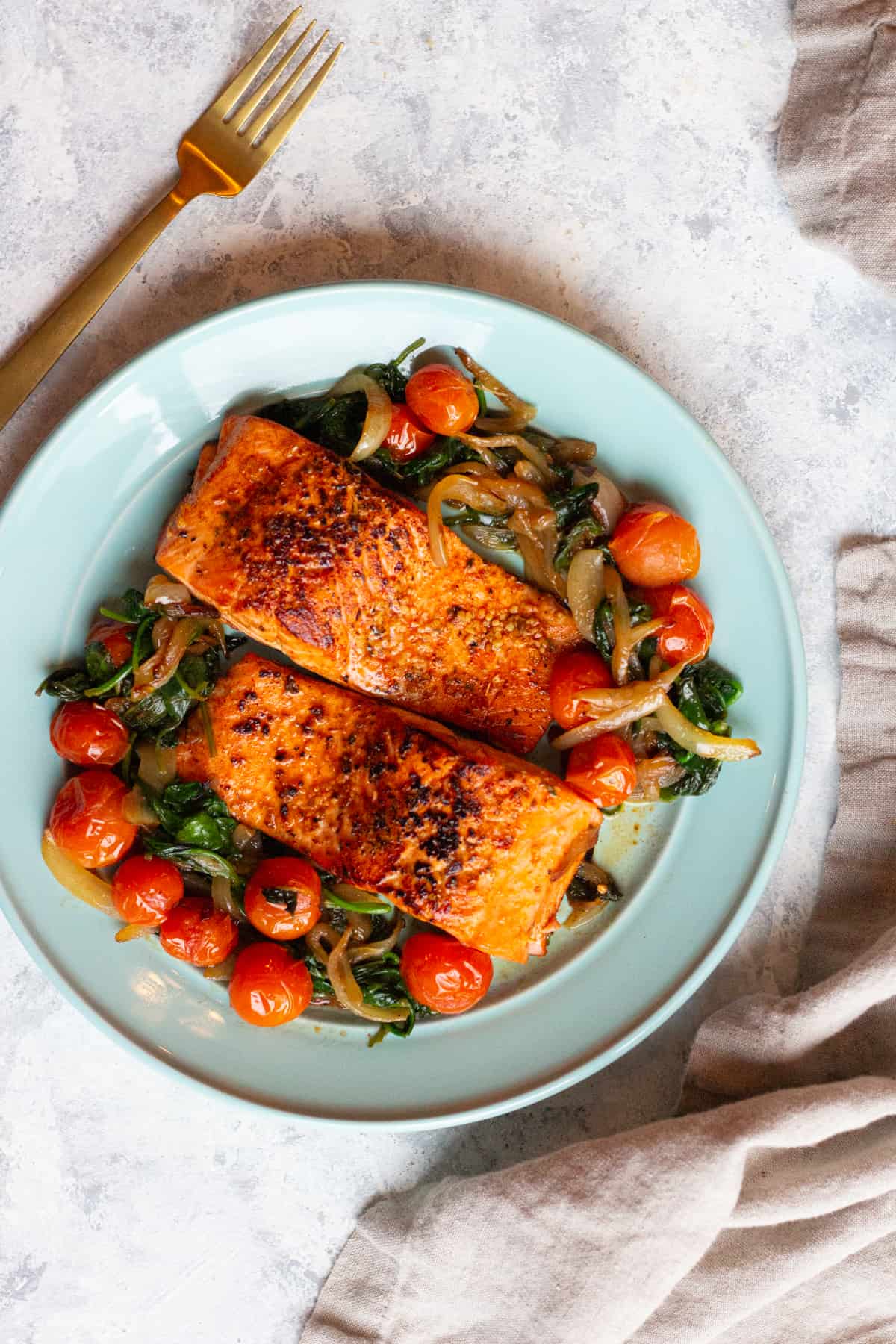 overhead shot of two salmon fillets with tomatoes and spinach. 