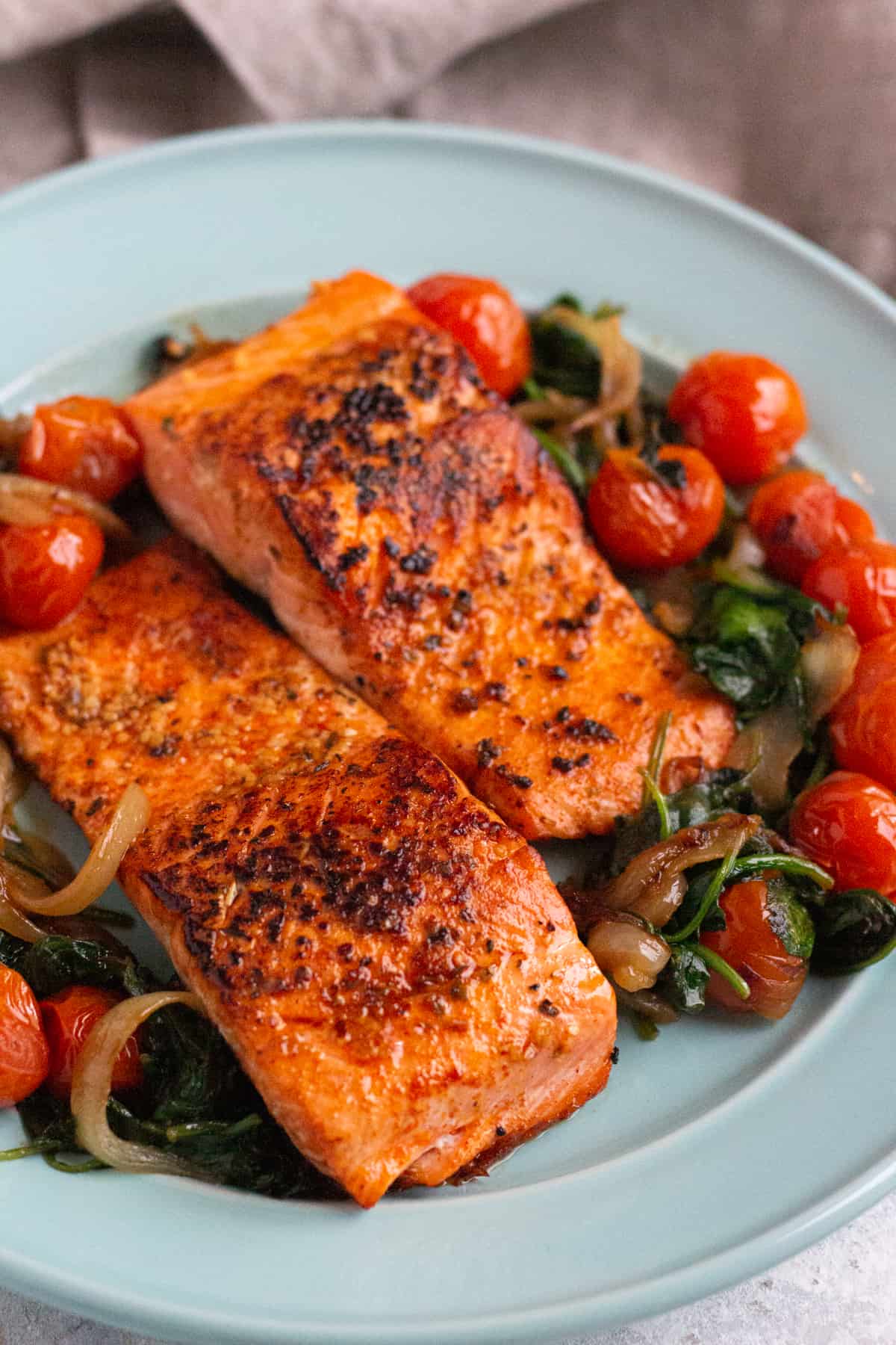 wo seared salmon fillets on a plate with cooked spinach and tomatoes.