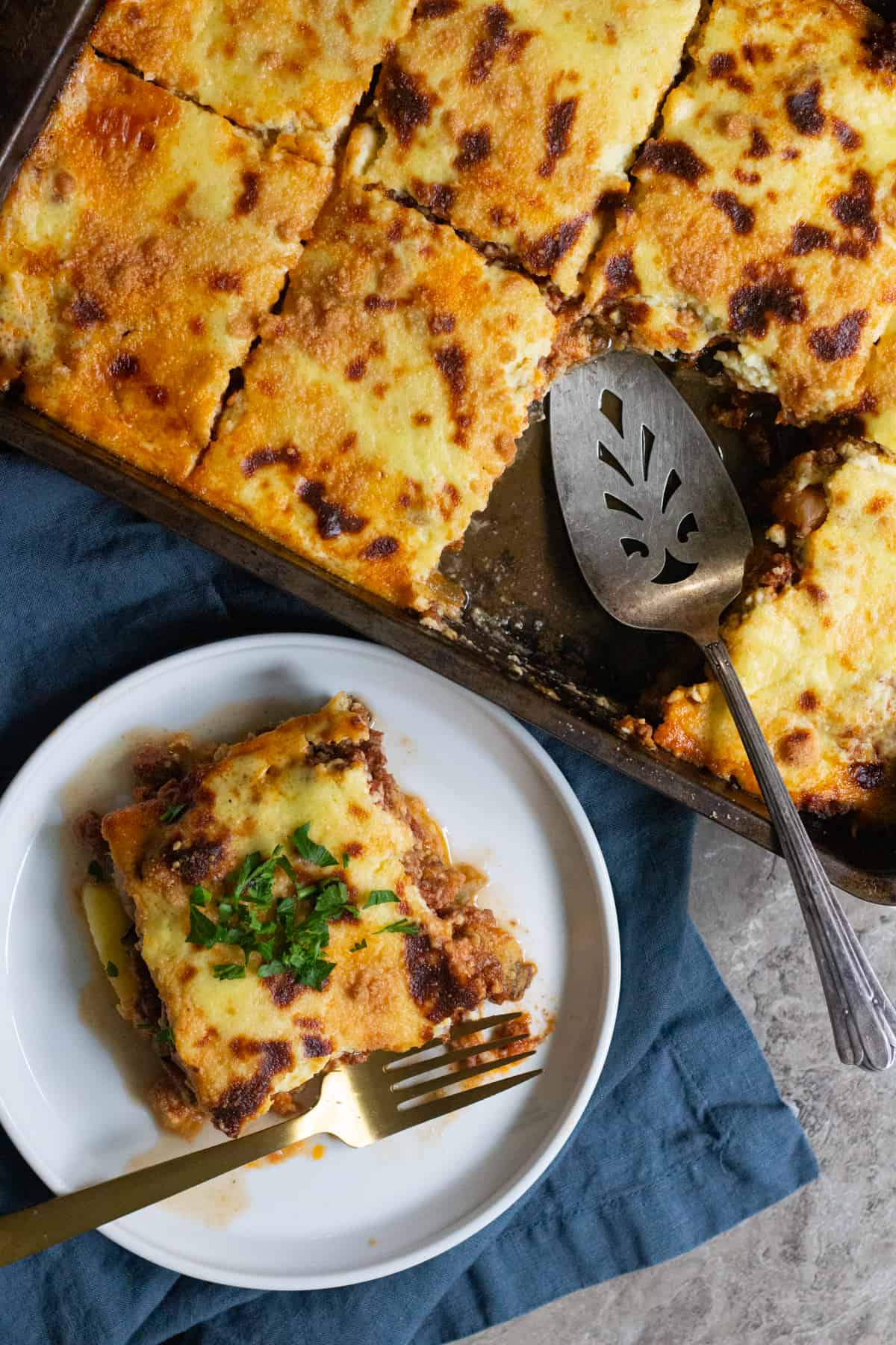 a slice of Greek eggplant moussaka on a plate and the rest in the pan.