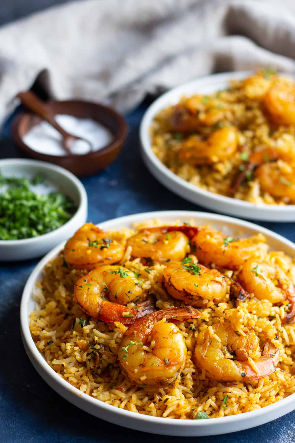 two shrimp and rice dishes on a blue surface with salt and cilantro and a napkin.