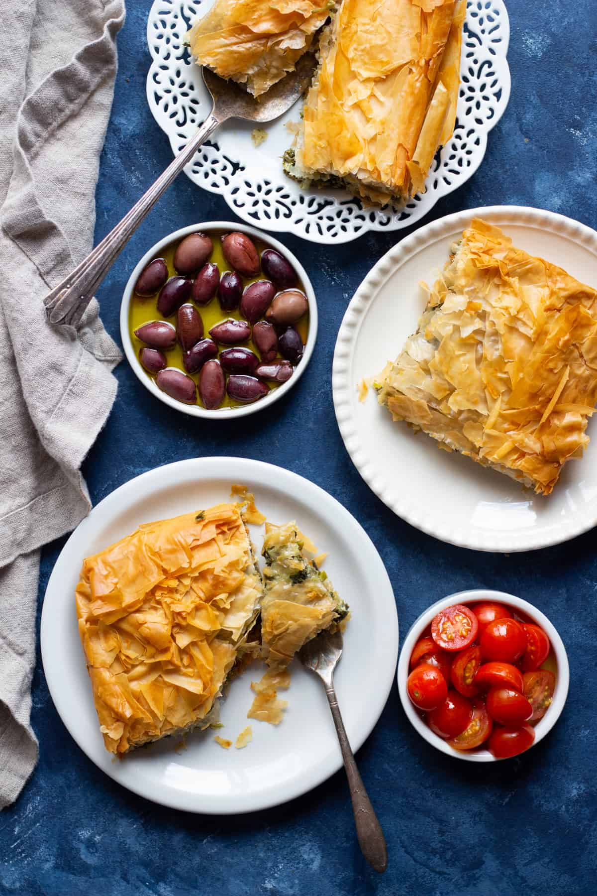Three plates of authentic spanakopita with olives in olive oil and tomatoes. 