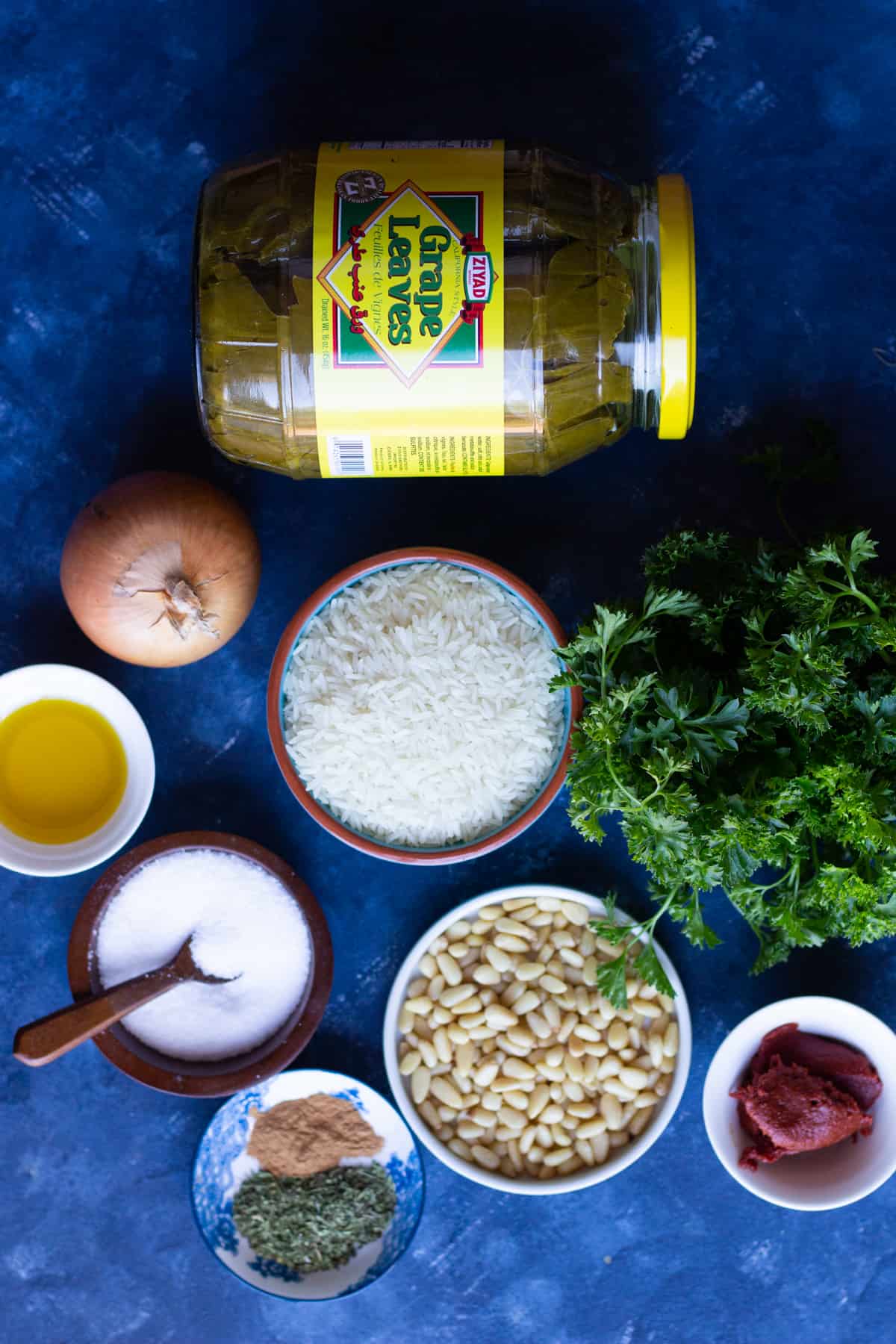 Ingredients shot for dolma recipe includes grape leaves, rice, onion, olive oil, parsley, spices, pine nuts and tomato paste