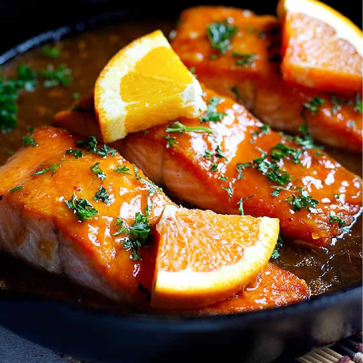 Salmon slices in a pan topped with orange glaze and slices of orange. 