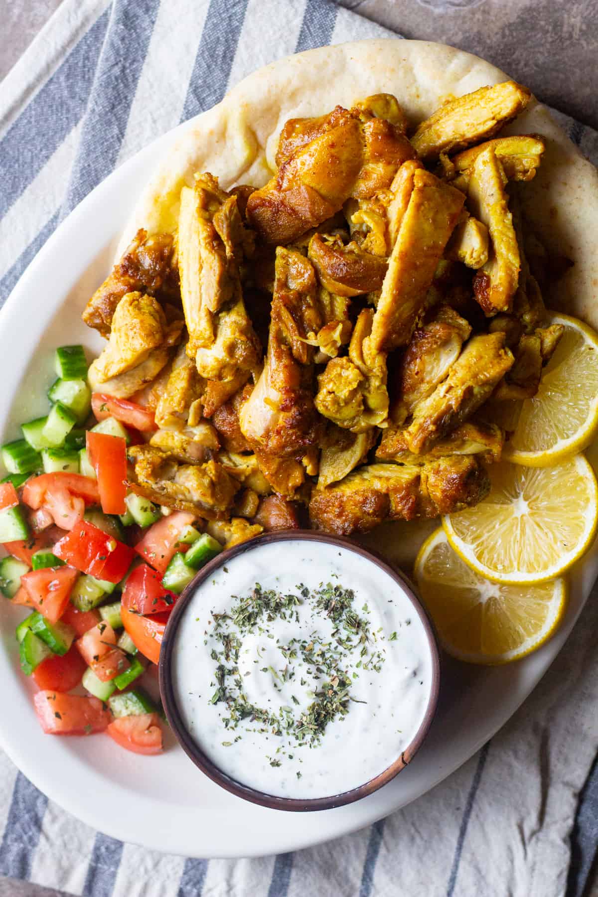 A platter of chicken shawarma with salad, yogurt sauce and lemon with fresh pita bread. 