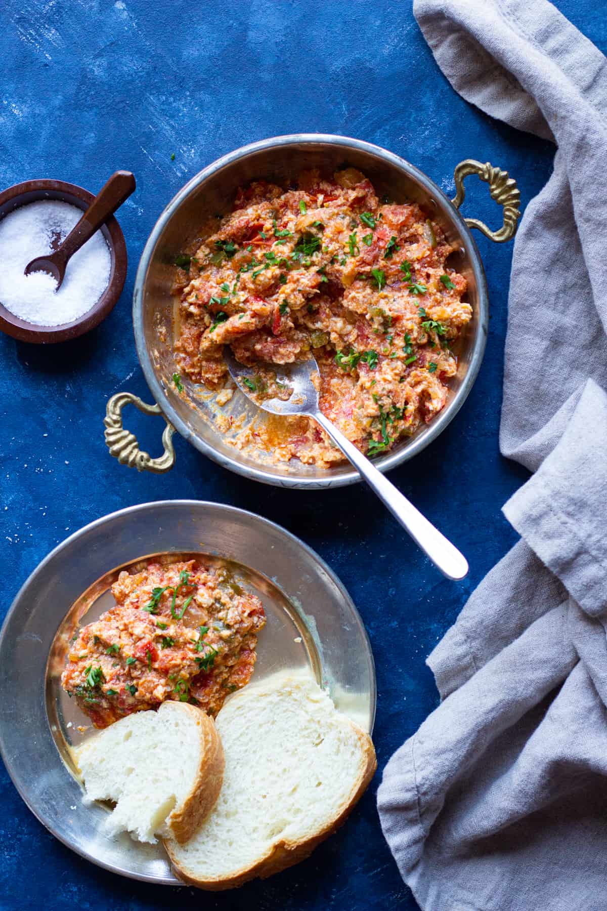 A pan of menemen with a plate full of menemen and some sliced bread. 