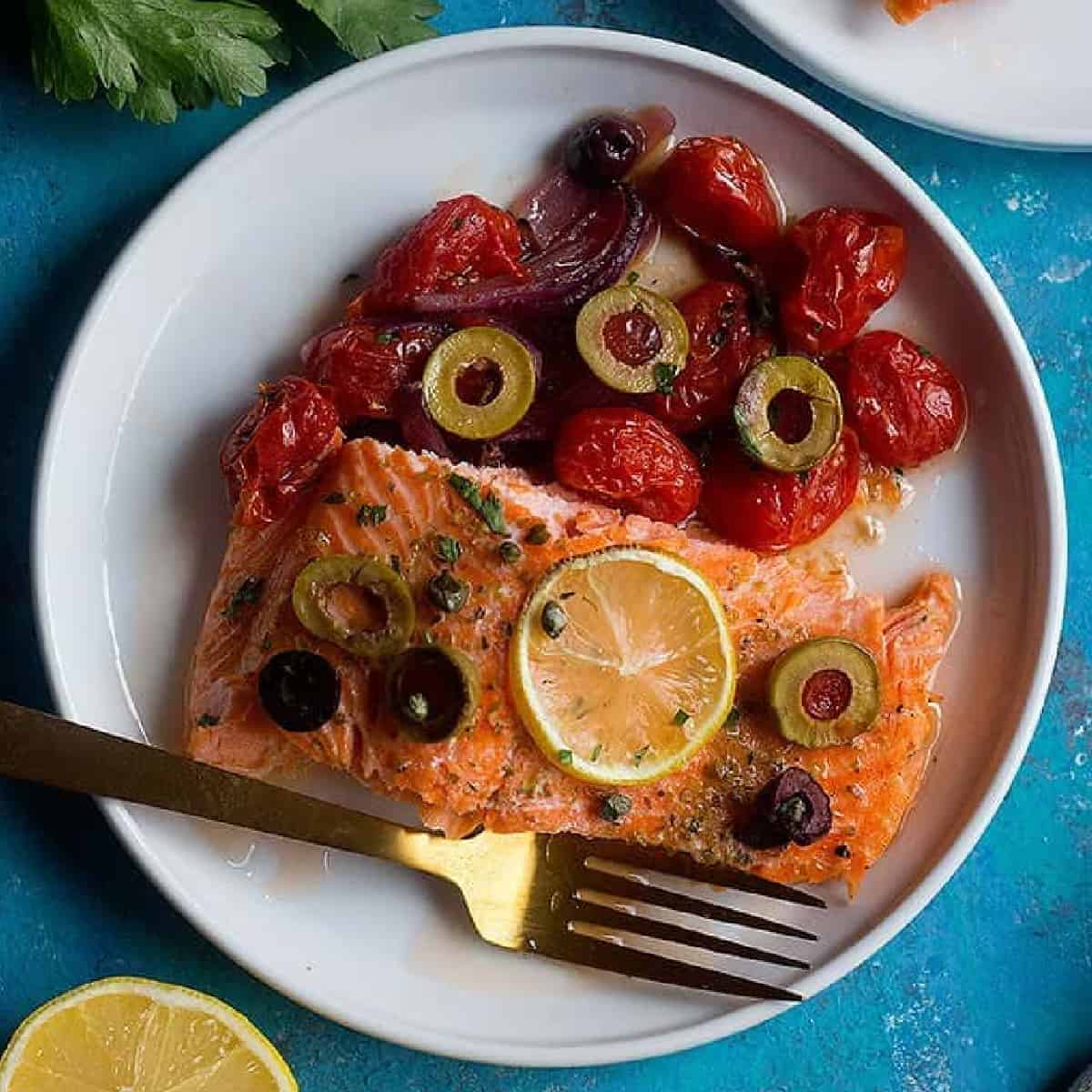 The best ever oven baked salmon is here! Flaky and moist Alaska salmon with olives and capers on a bed of vegetables is the best weeknight dinner!
