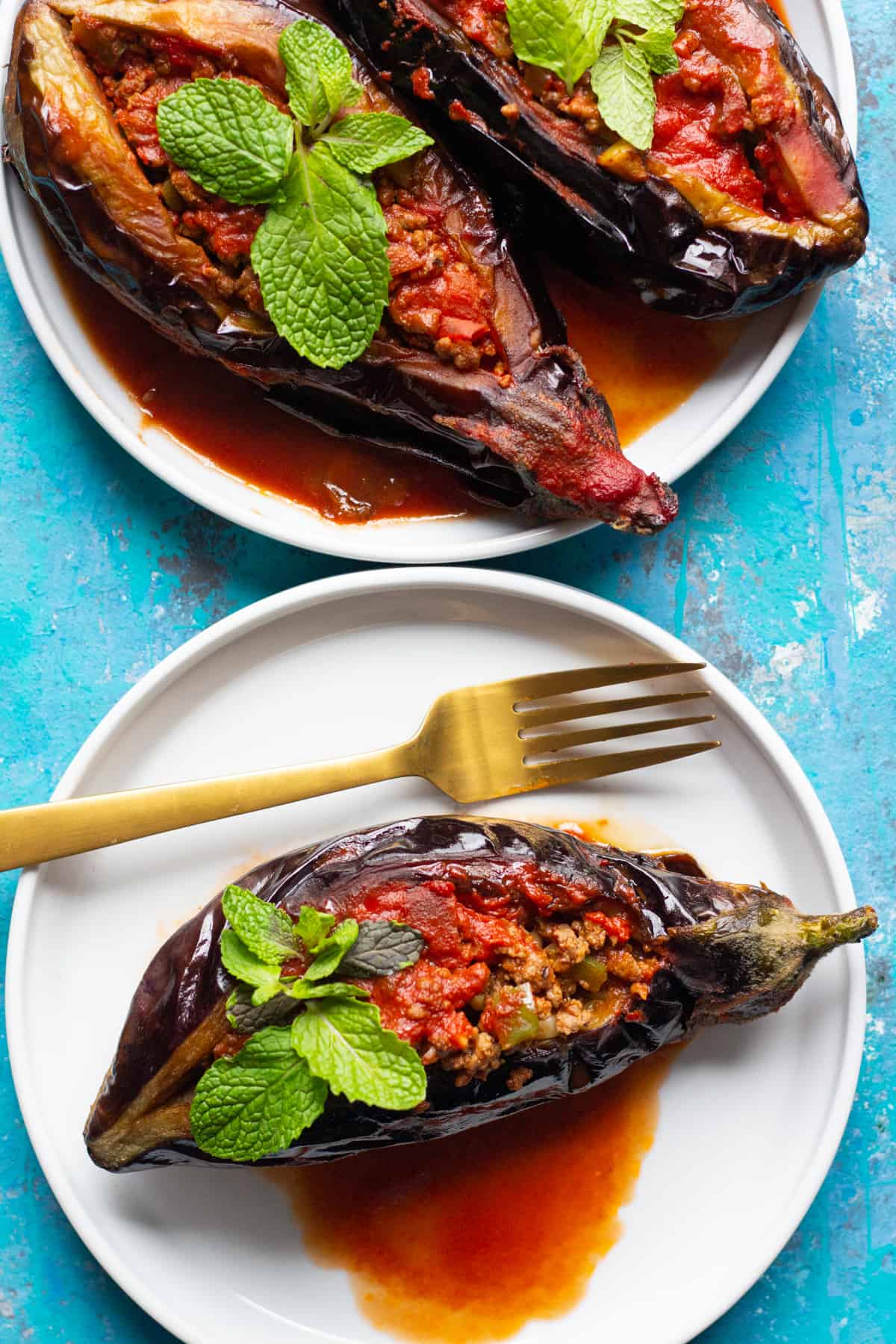 Turkish stuffed eggplant on white plates topped with fresh mint. 