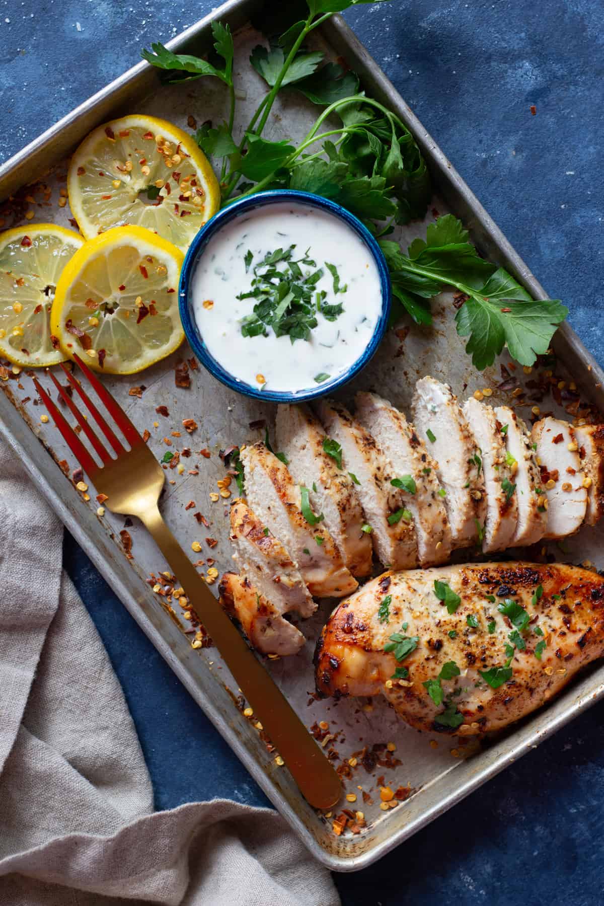 A tray with baked Greek chicken sliced and topped with parsley. 