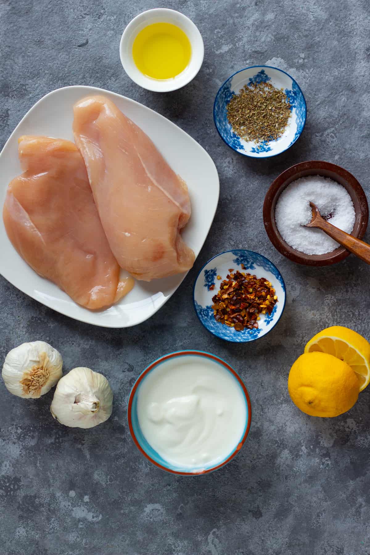 Ingredient shot for the recipe including olive oil, oregano, chicken, pepper, salt and lemon. 