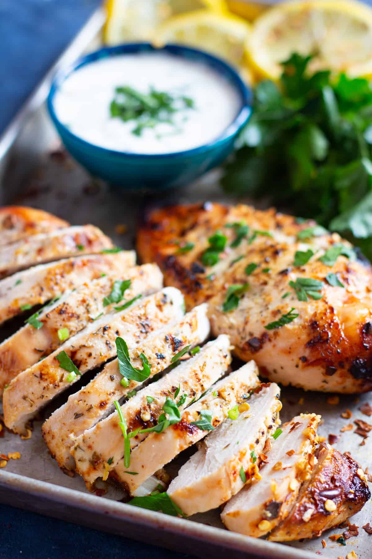 Two baked chicken breast on a tray. One is sliced and one is left whole. 