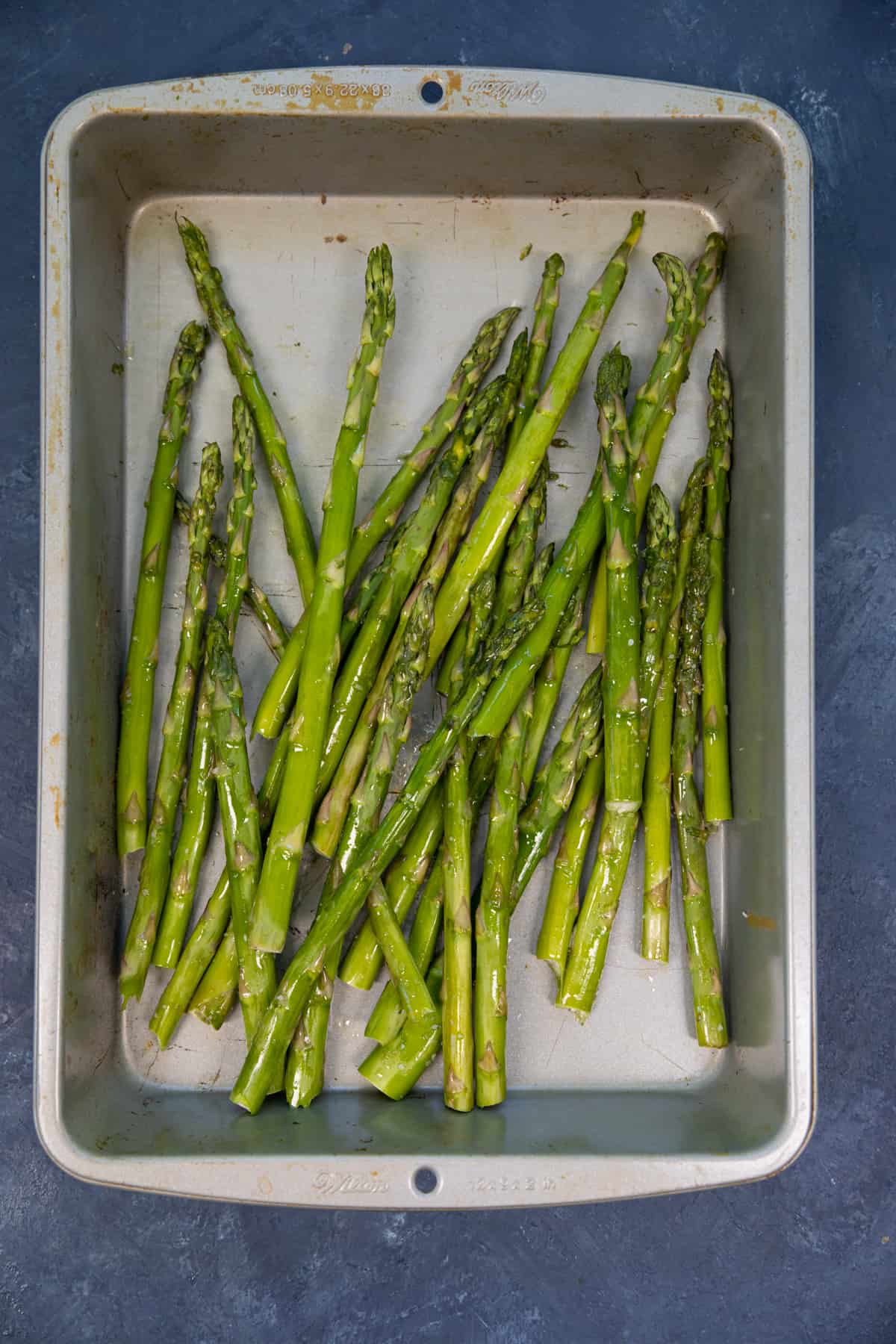 Asparagus coated with olive oil in a pan. 