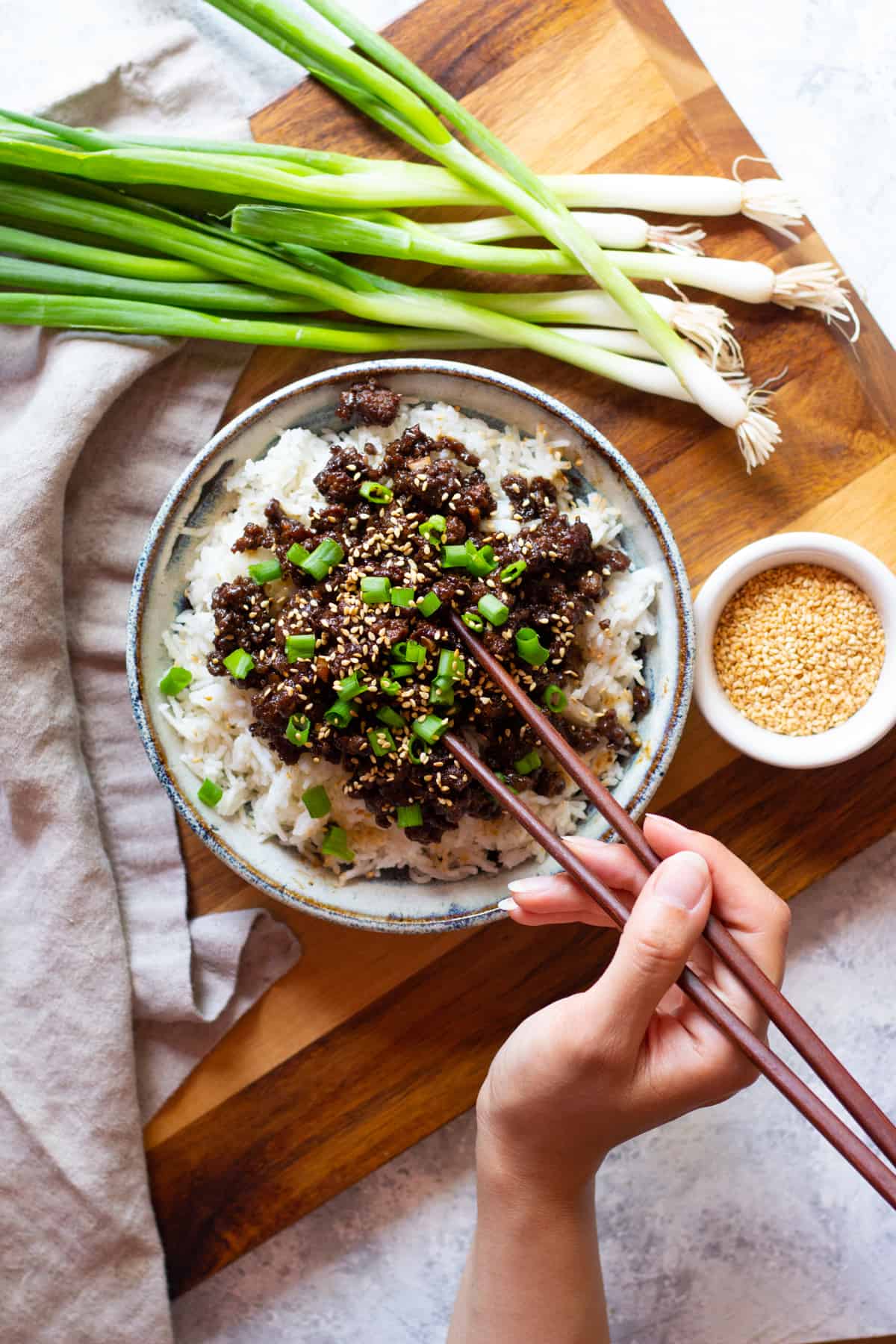 A bowl of Korean style beef and rice on a wooden board eaten with chopsticks.