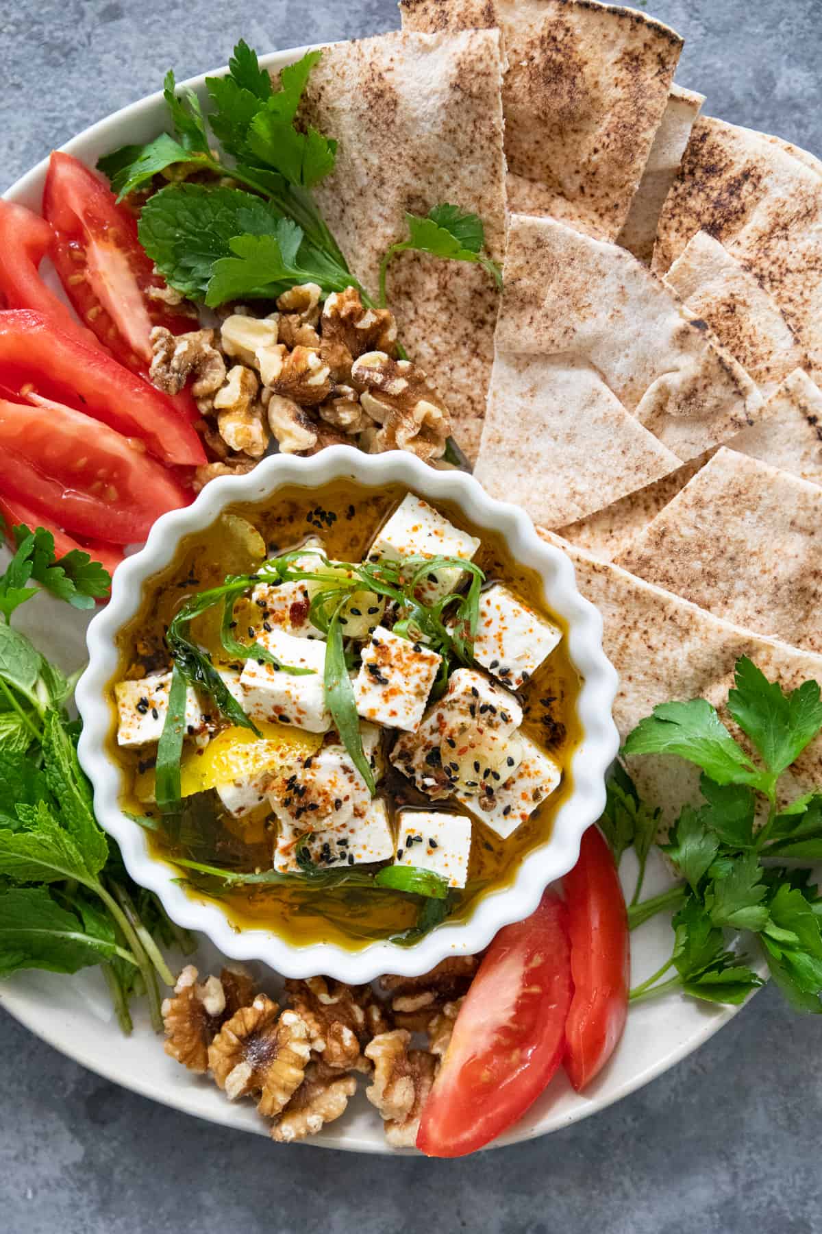 overhead shot of marinated feta with pita chips, walnuts, tomatoes and herbs.