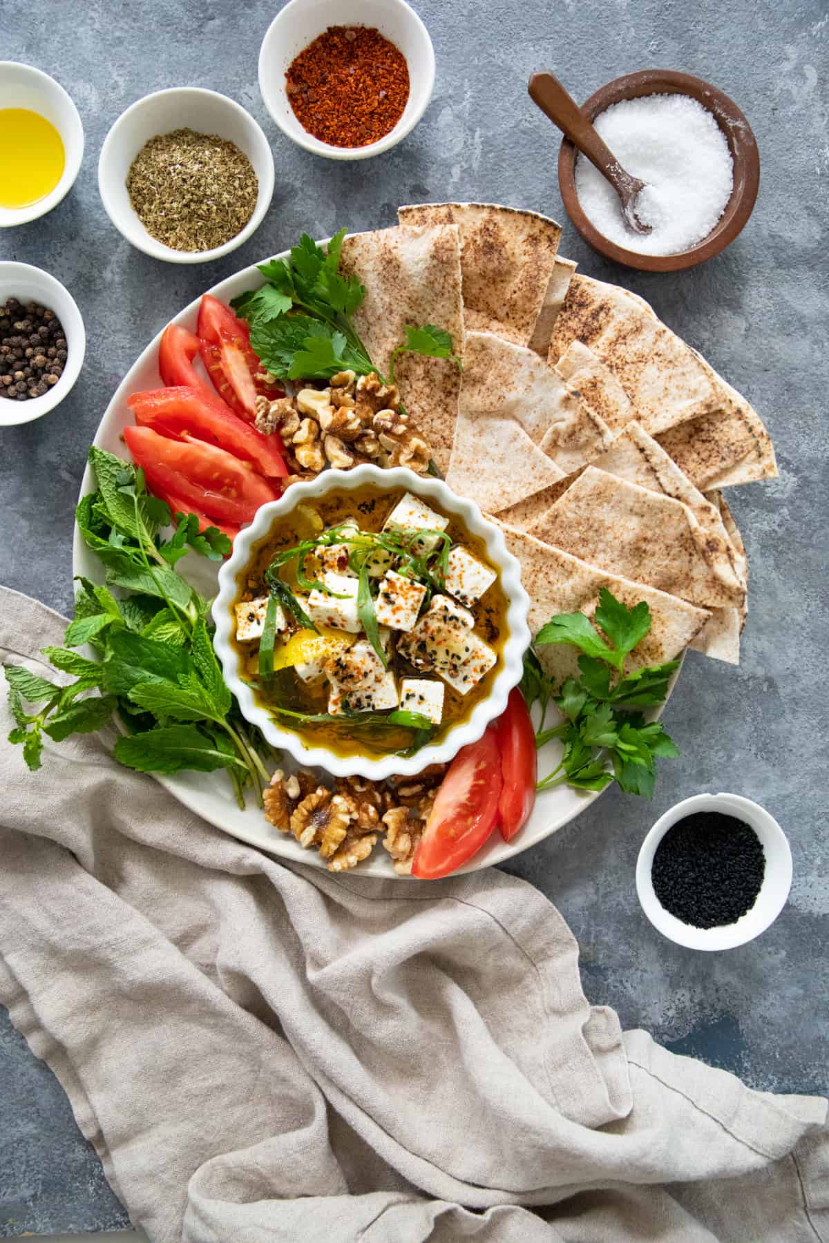 overhead shot of a plate with pita, feta, walnuts, tomatoes and herbs. 