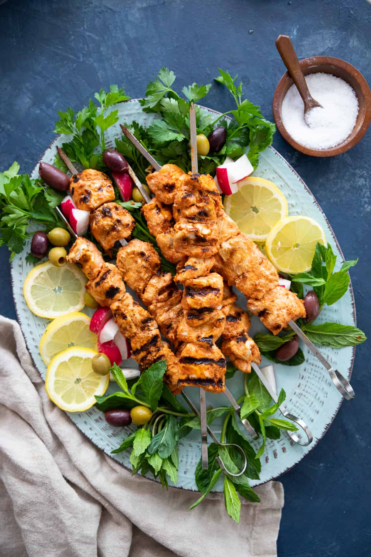 grilled chicken kabobs on a platter with herbs and vegetables. 