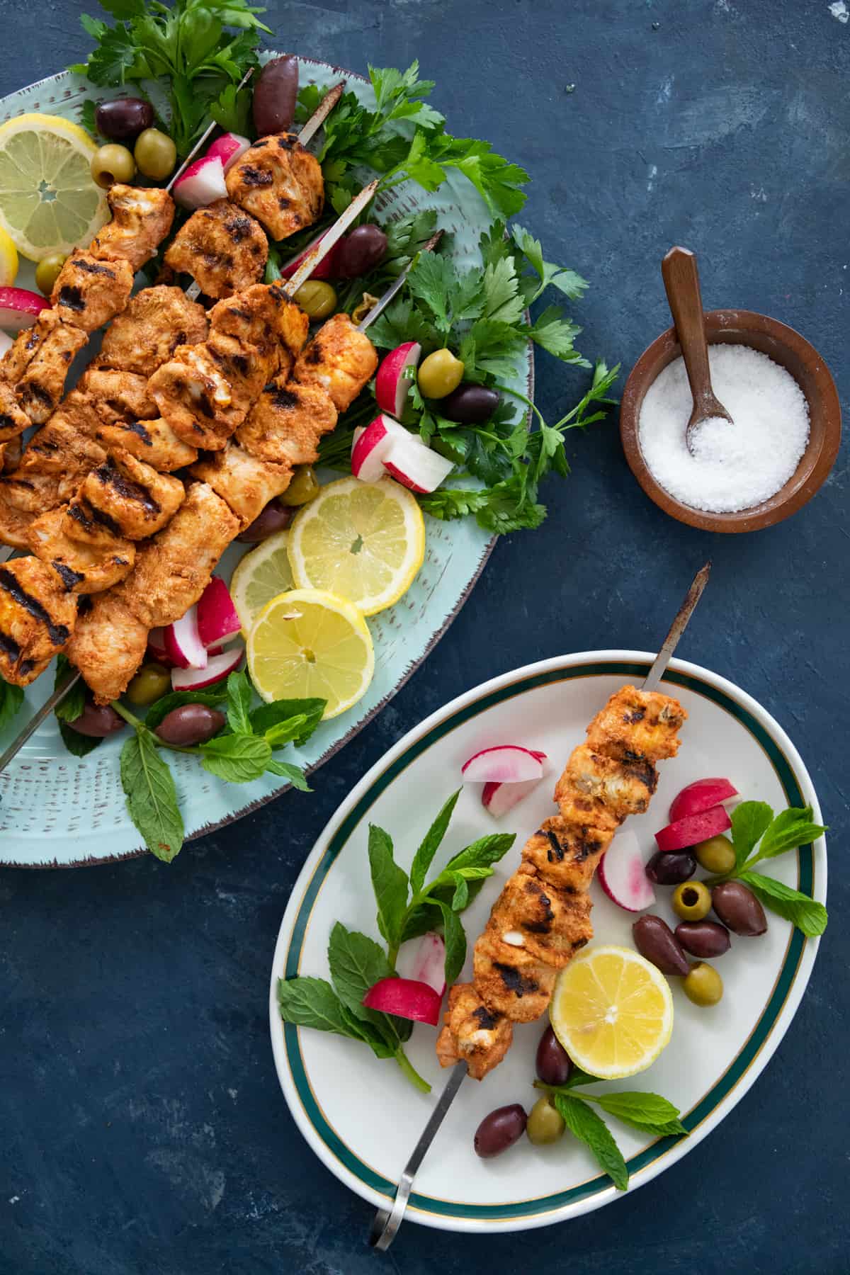 a skewer of grilled chicken on a platter with herbs and vegetables. 