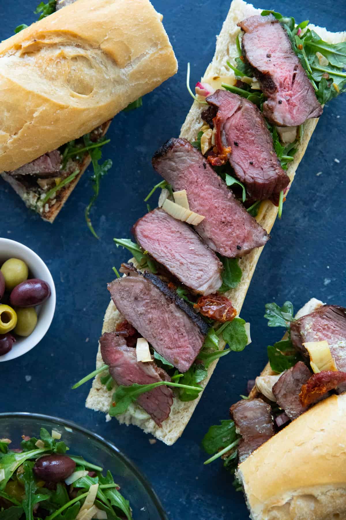 slices of grilled steak on a piece of baguette with vegetables. 