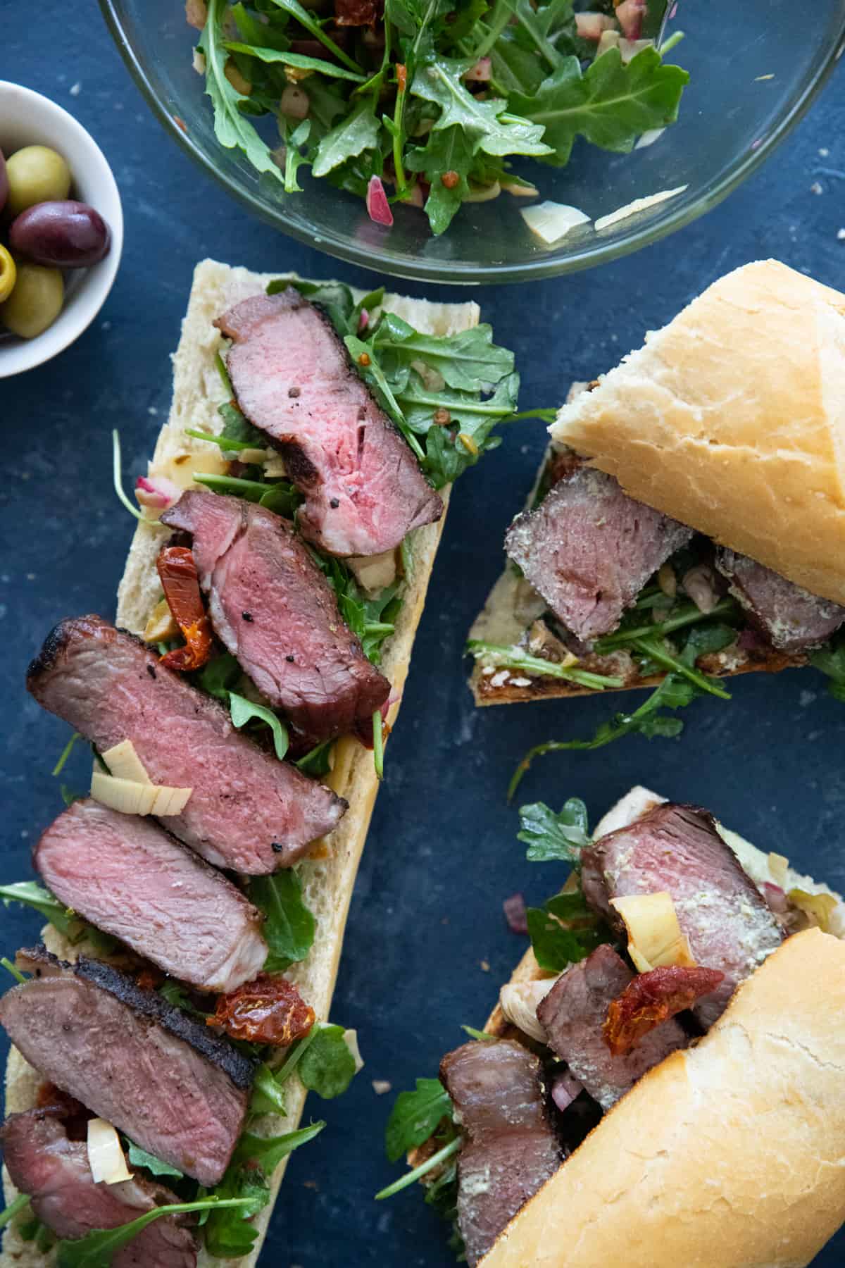 Grilled steak sandwich on a blue backdrop. 