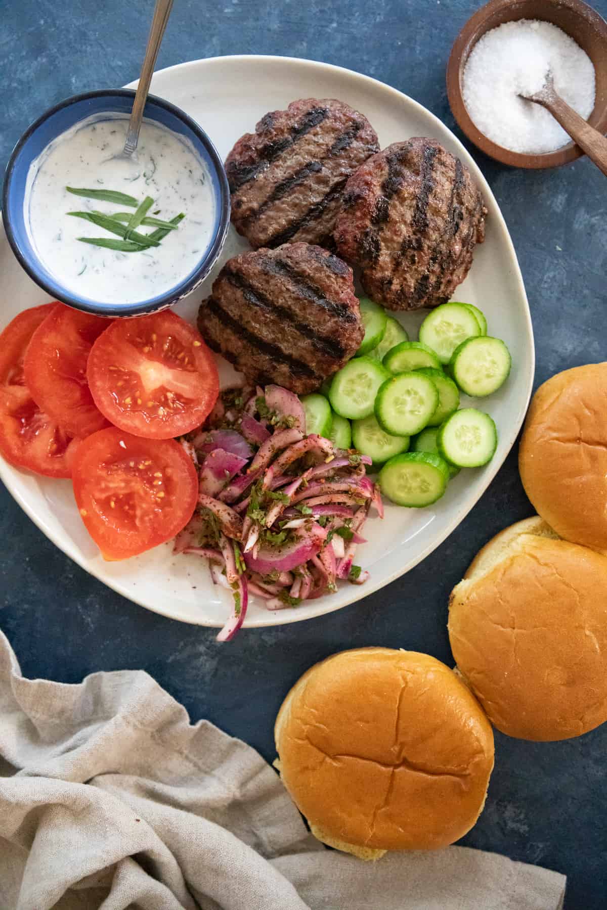 grilled lamb burgers on a plate with tomatoes, cucumbers and sumac onions. 