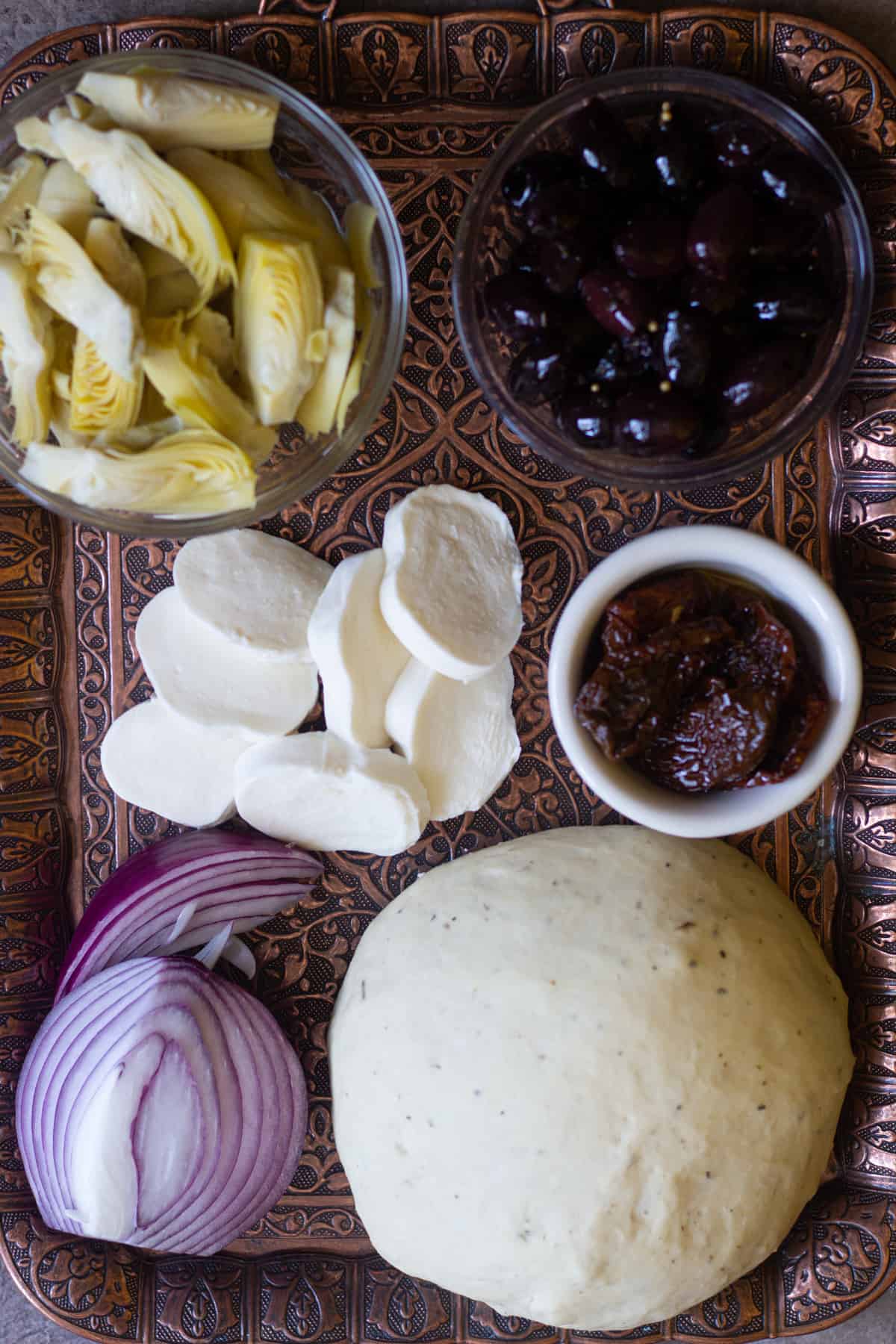 Mediterranean pizza ingredients are pizza dough, red onion, artichokes, kalamata olives, sun dried tomatoes and mozzarella