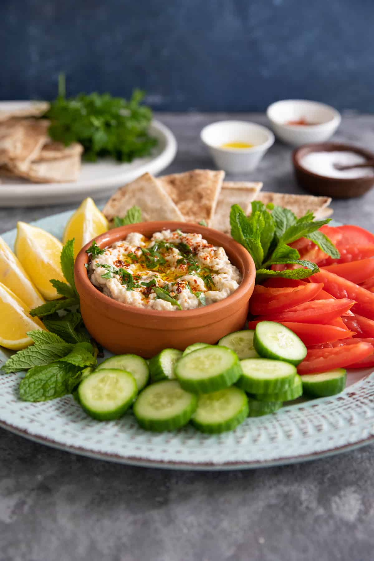 shot of moutabal on a blue platter with pita and vegetables. 