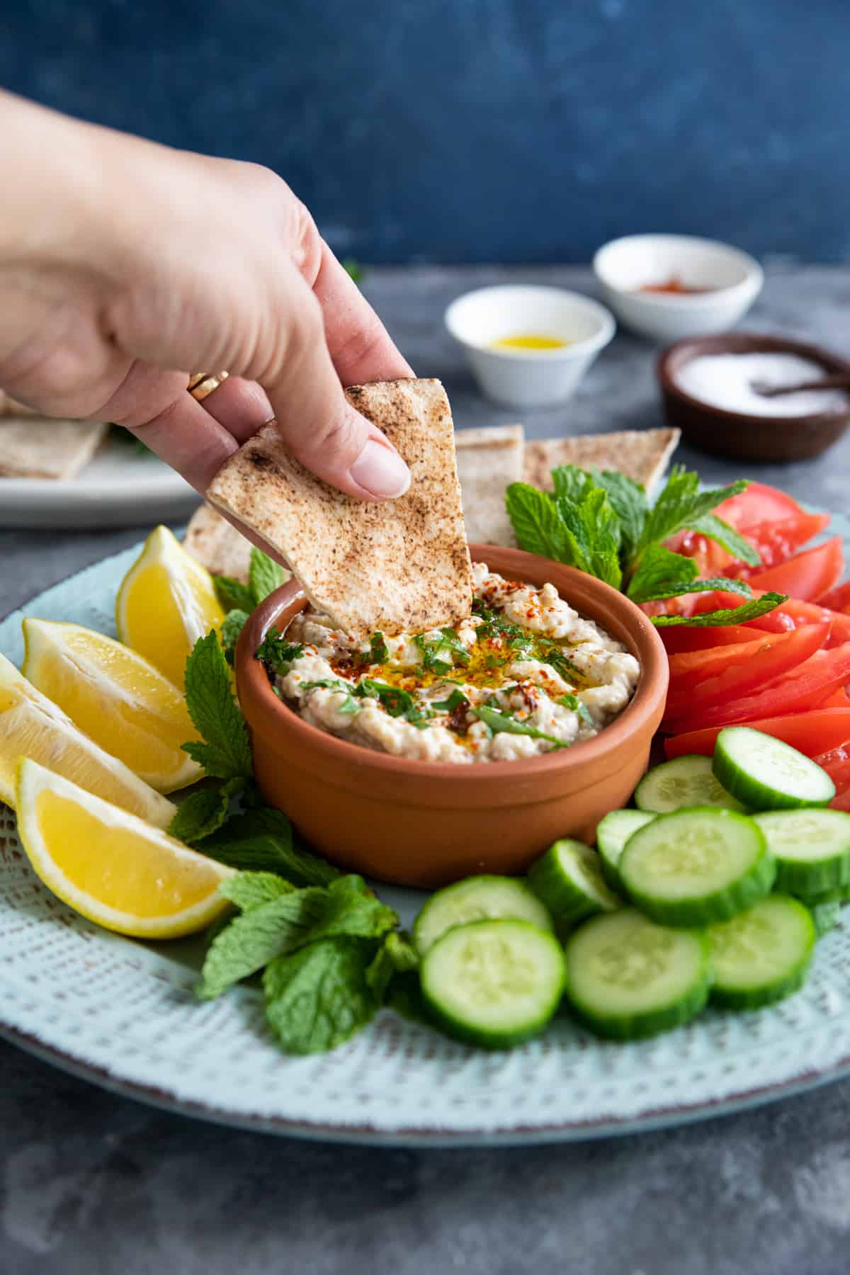 shot of smoky eggplant dip with a hand dipping a piece of pita bread. 