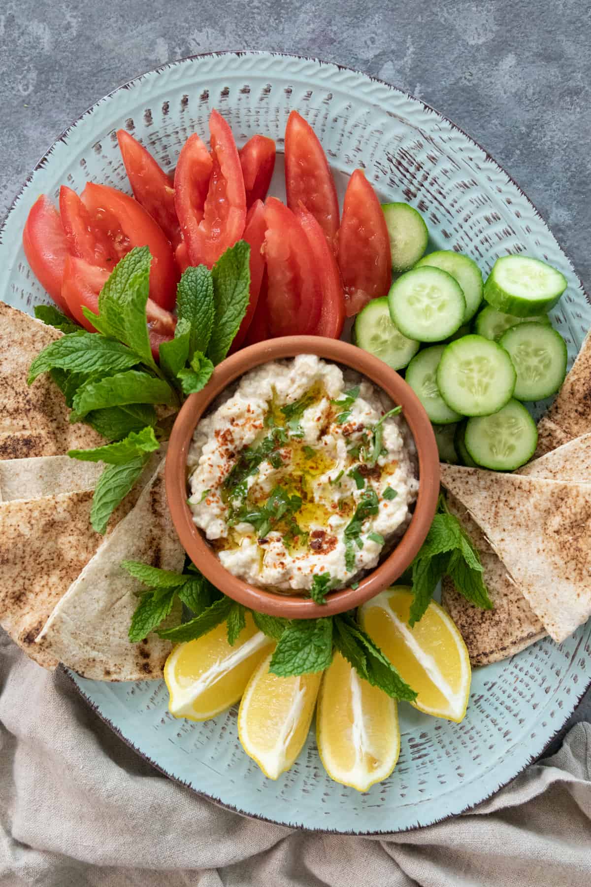 overhead of mutabal on a platter with pita, herbs and tomatoes.